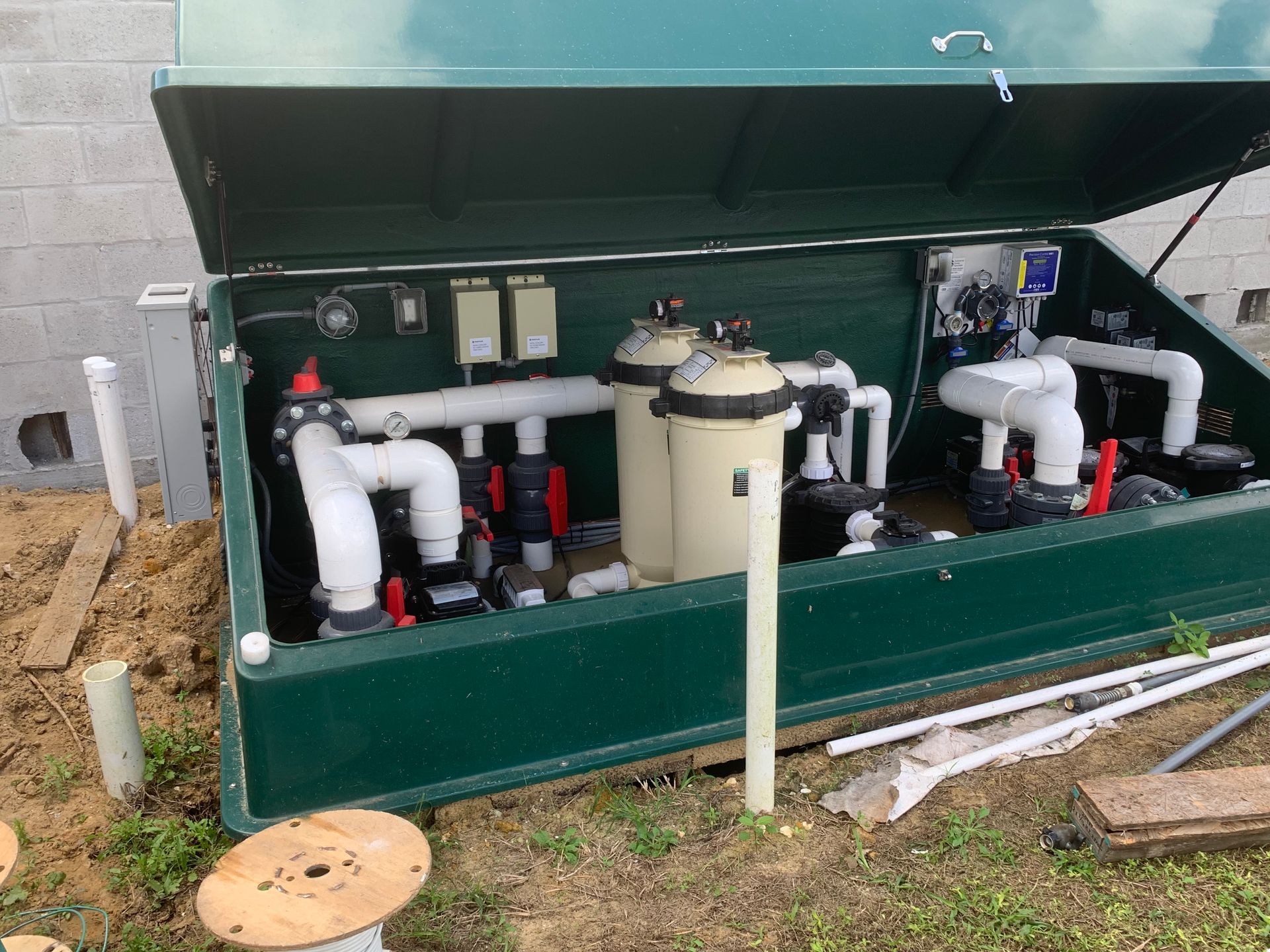 Open green utility cabinet with pipes, filters, and valves installed outdoors beside a building.