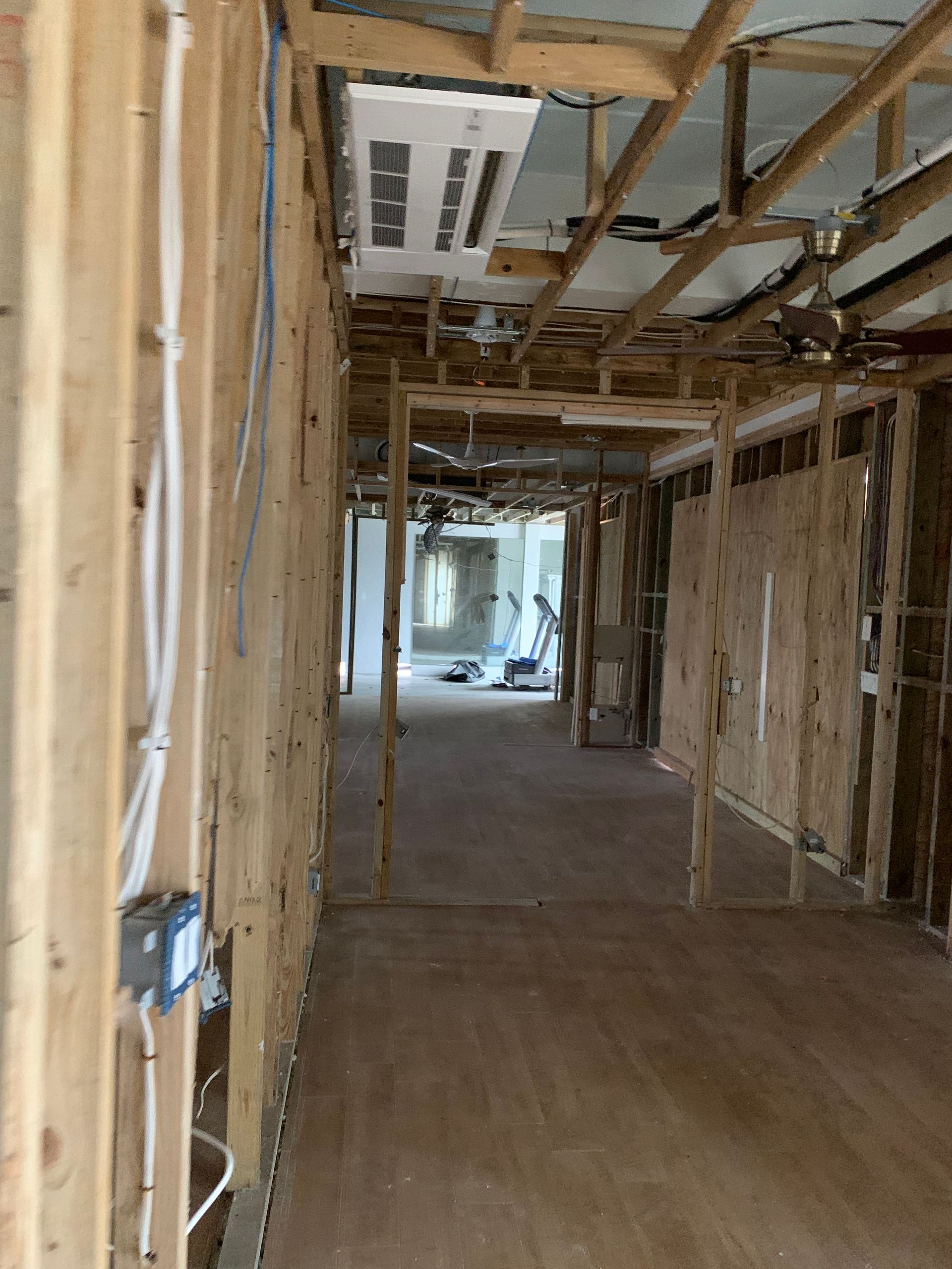 Unfinished interior hallway with exposed wooden framing and drywall, leading to a bright opening at the far end.