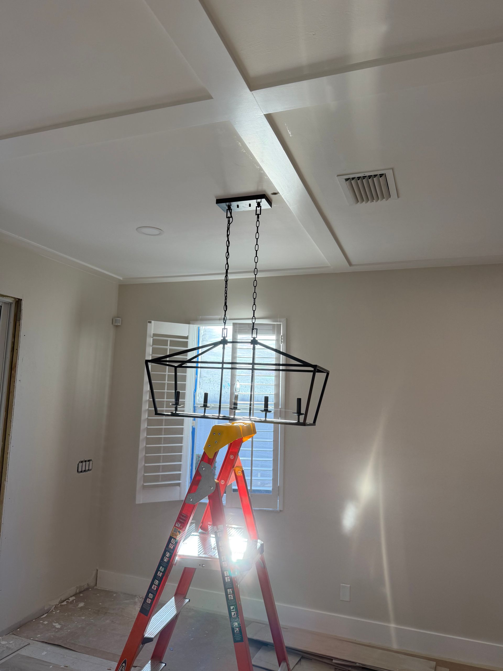 Red ladder under a hanging light fixture in a room with white walls and ceiling panels.