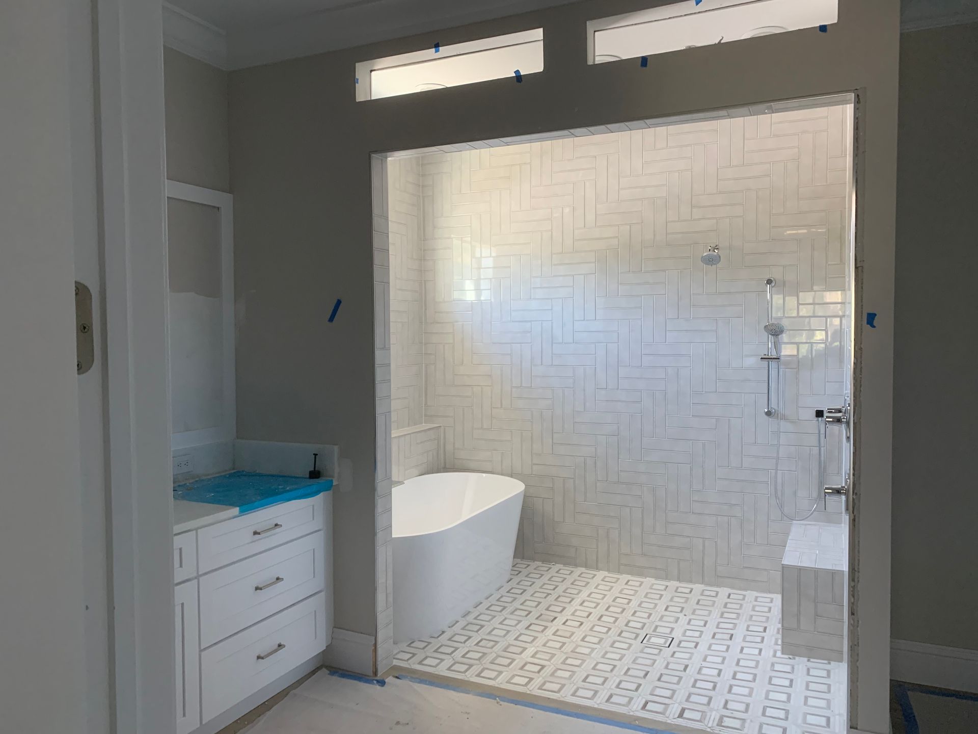 Modern bathroom with tiled shower, bathtub, vanity, and soft overhead light.