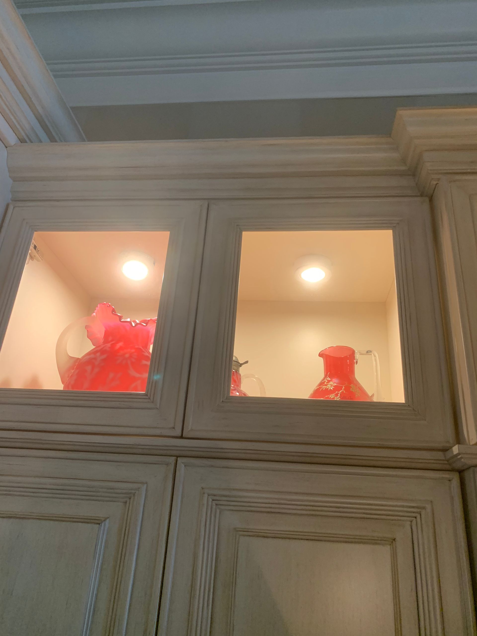 Wooden cabinet with lit glass-front upper compartments displaying red vases and decor