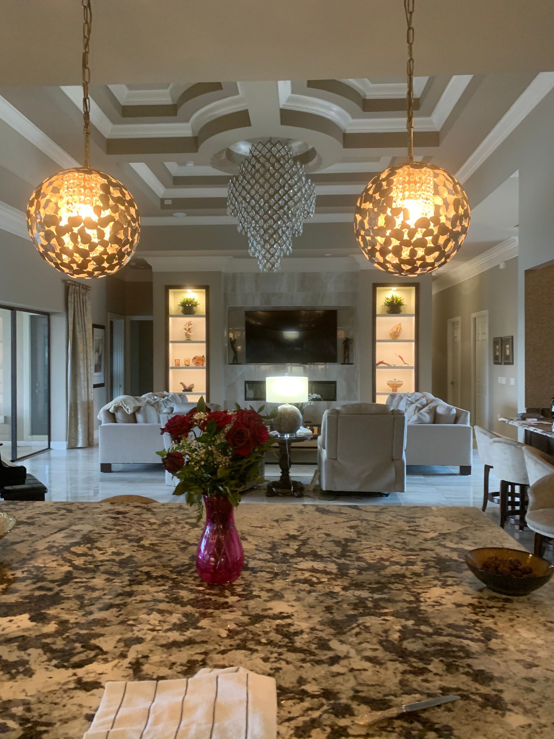 Modern living room with chandelier lights, marble island, TV, and floral centerpiece on the counter