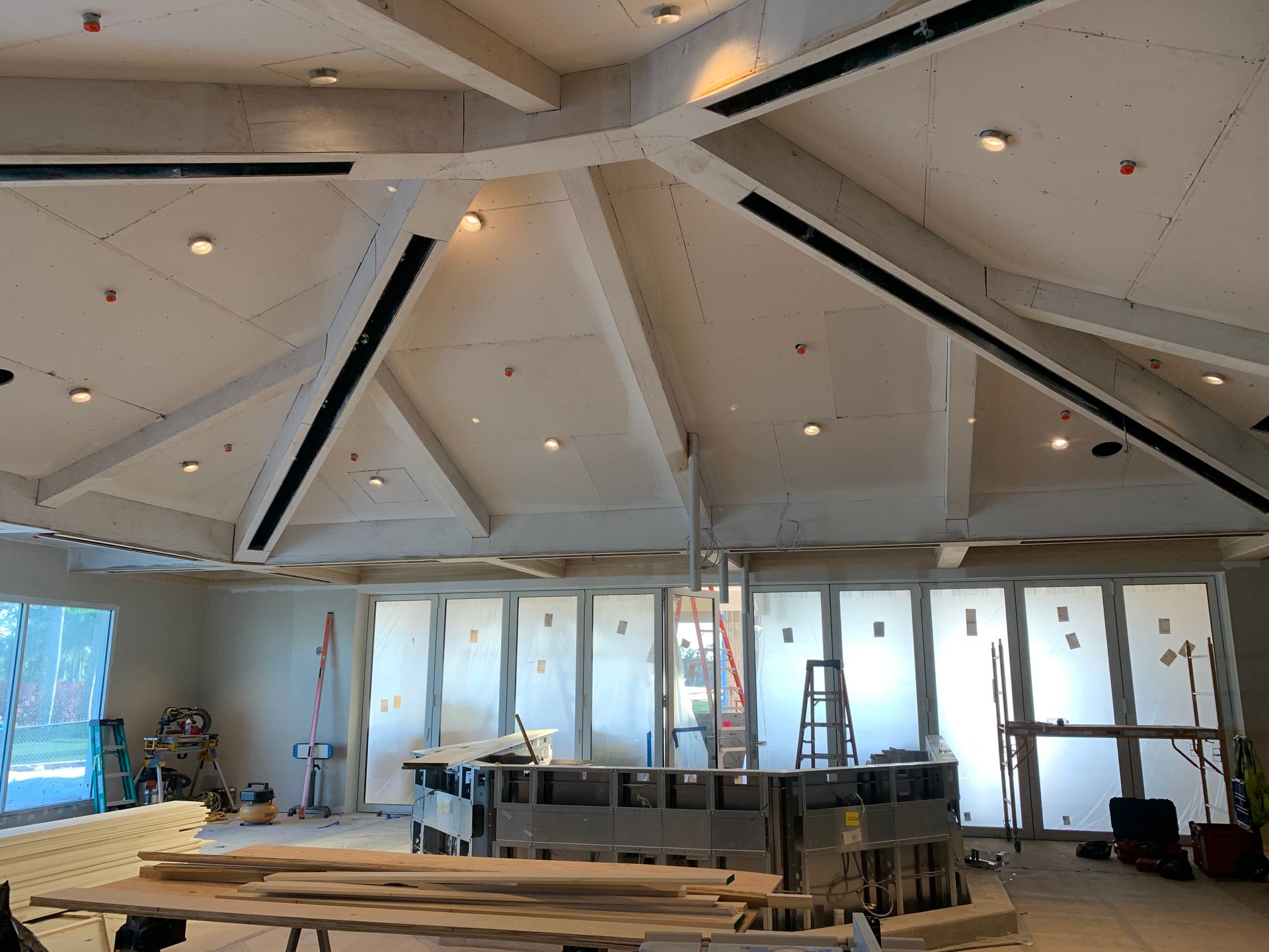 Partially renovated room with a vaulted ceiling, windows, ladders, and construction materials