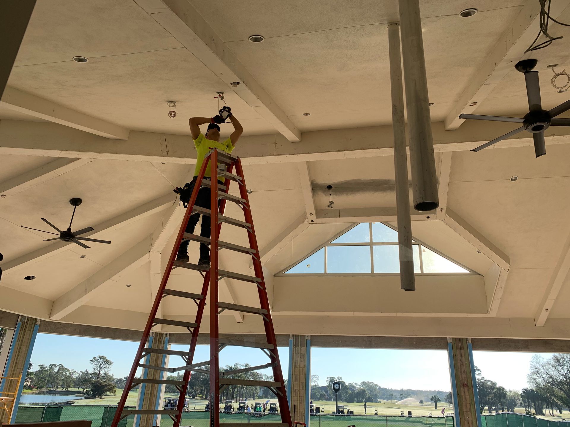 Worker on a red ladder repairing the ceiling of a pavilion with exposed beams.