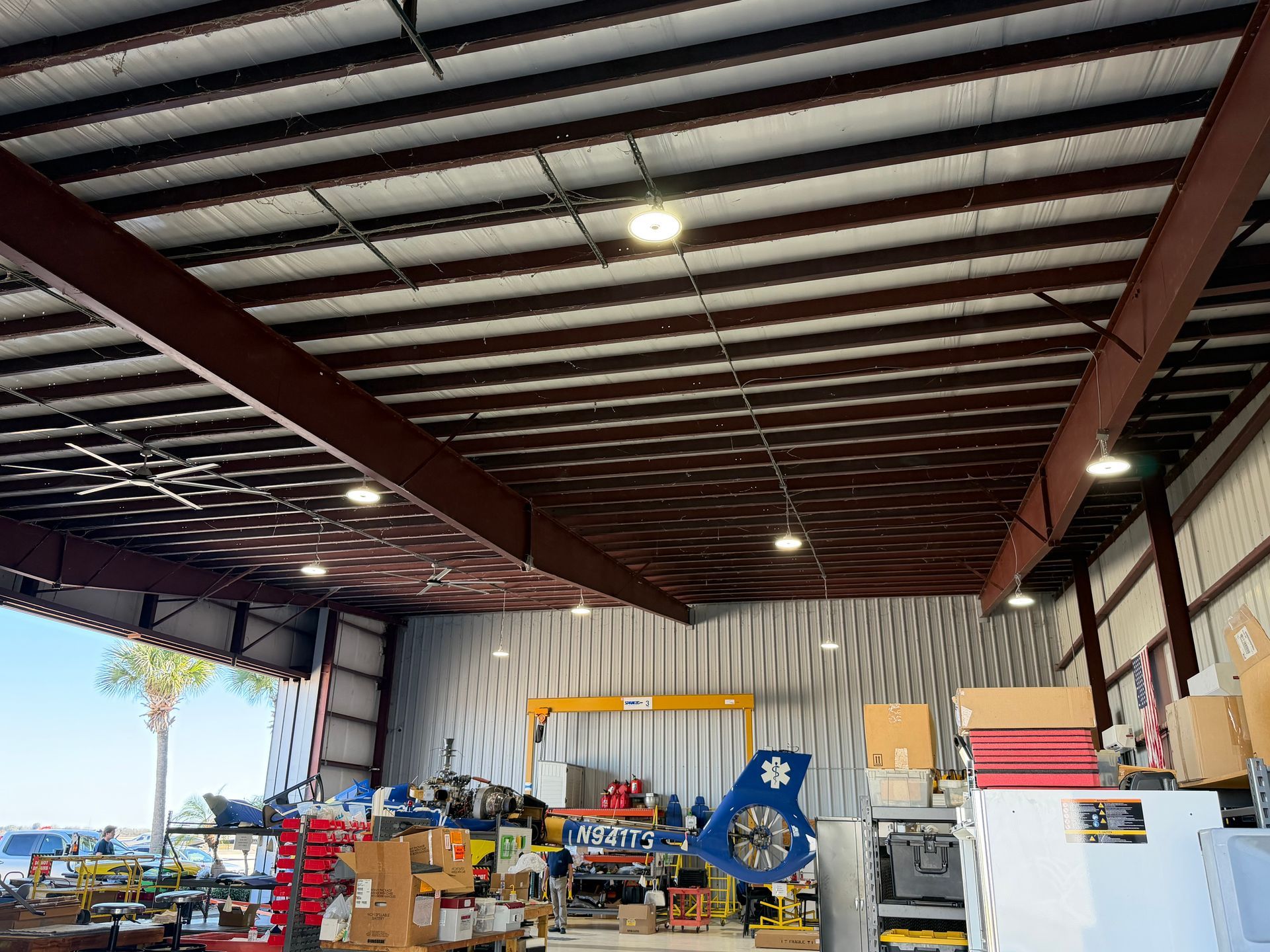 Interior of a warehouse workshop with steel beams, tools, equipment, and a large open doorway to the outside