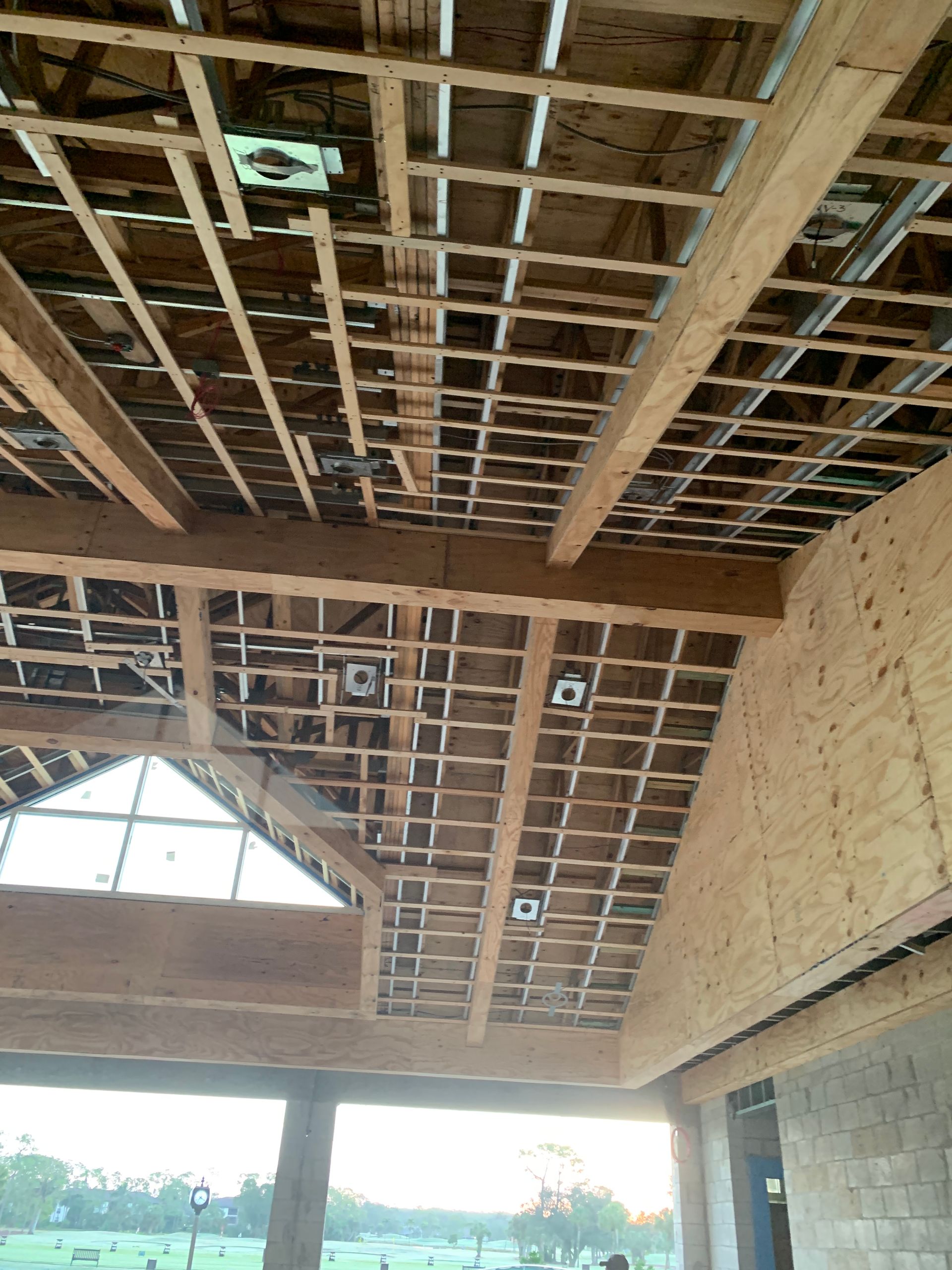 Interior of unfinished building with exposed wooden roof beams and a large open wall view outside.