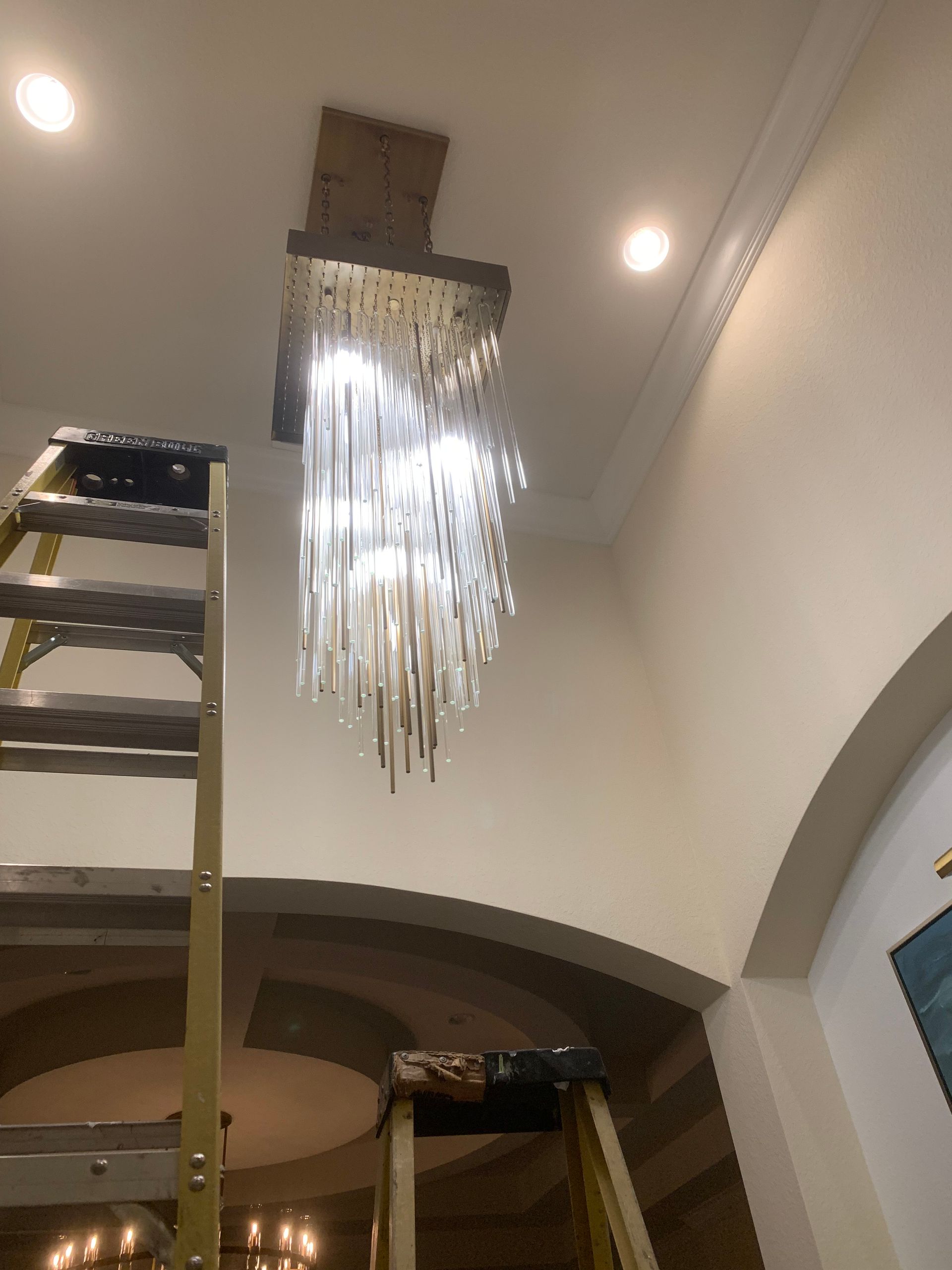 Chandelier hanging from a ceiling inside a room, with a ladder beside it during installation or repair.