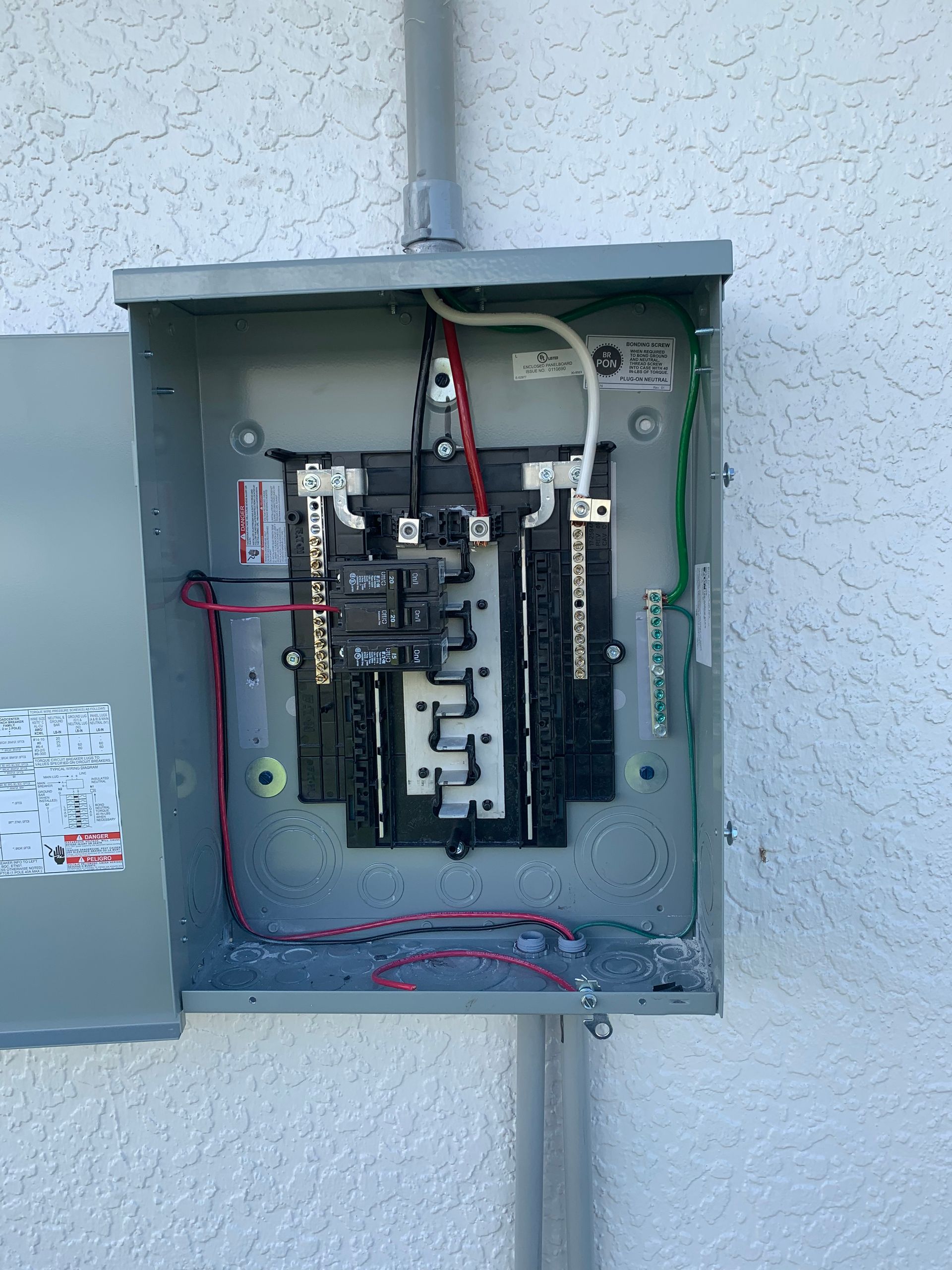 Open electrical panel mounted on an exterior wall with wires and breakers exposed