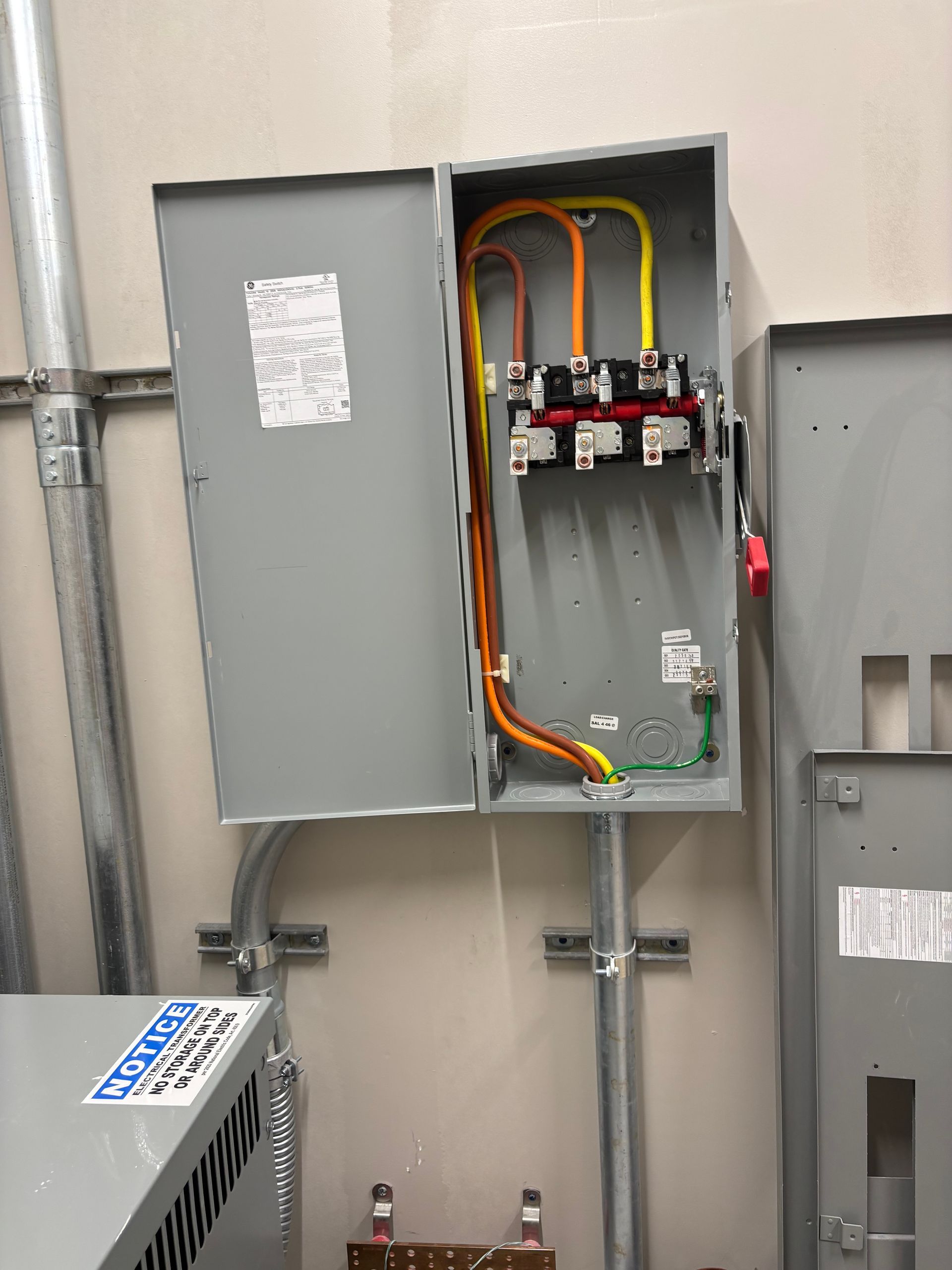 Open electrical breaker panel with orange wiring and gray metal cabinet in a utility room.