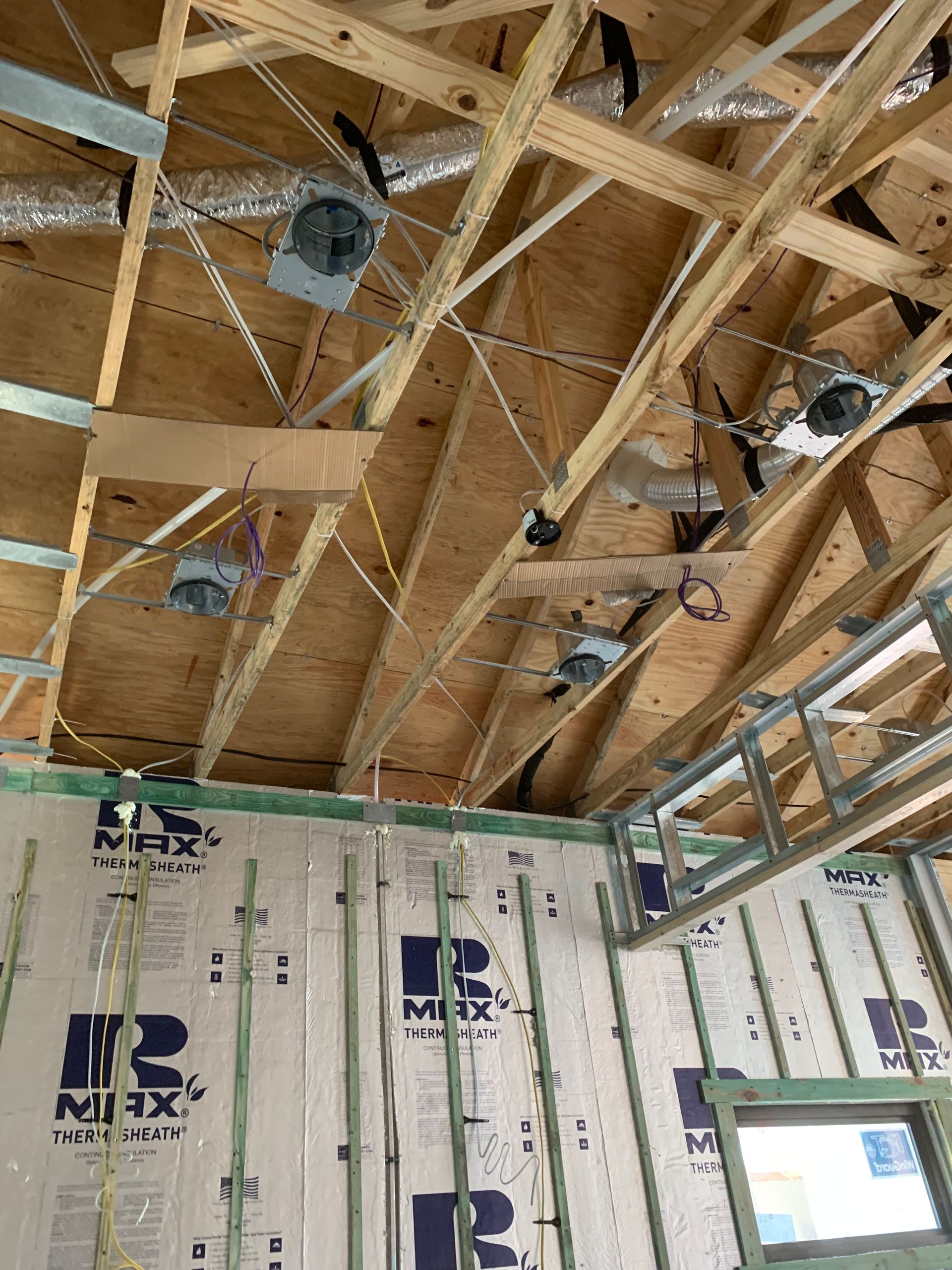 Unfinished room with exposed wooden rafters, insulation panels, hanging lights, and a window opening.