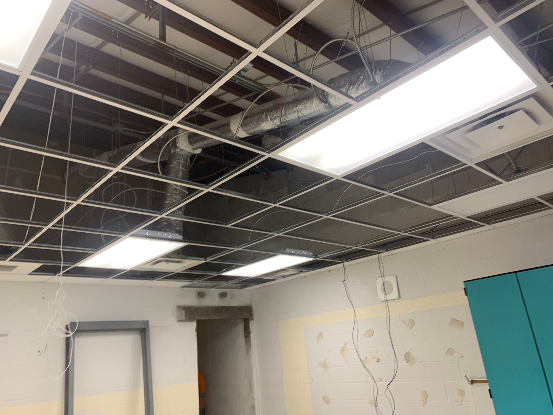 Damaged ceiling with exposed grid, fluorescent lights, and hanging wires in a room under renovation
