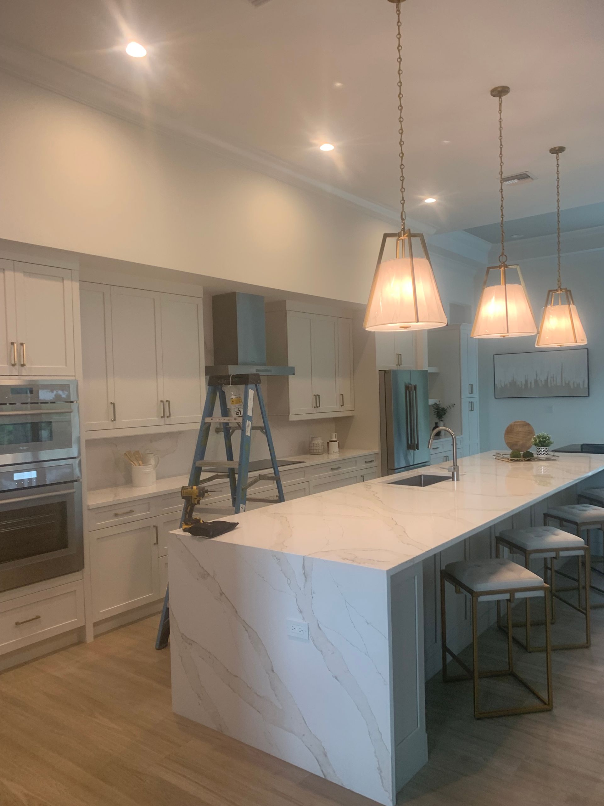 Modern kitchen with white marble island, pendant lights, and a step ladder under installation work