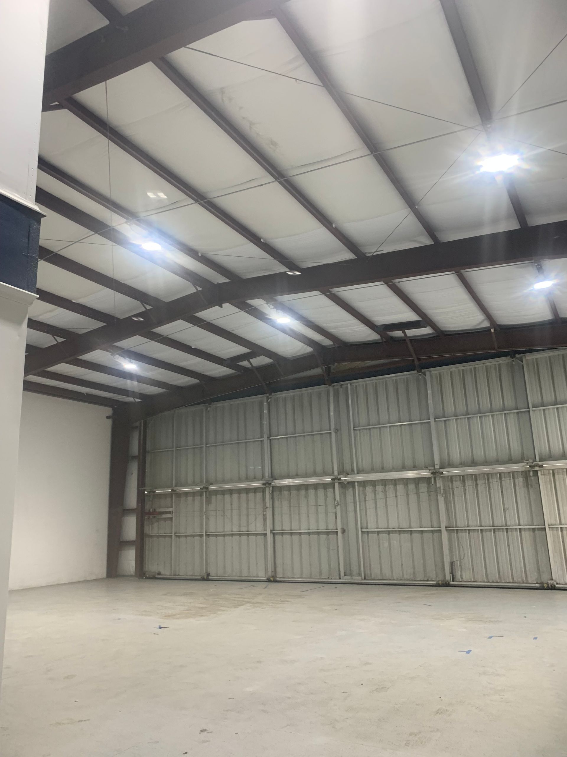 Empty warehouse interior with a concrete floor, metal walls, and bright overhead lights