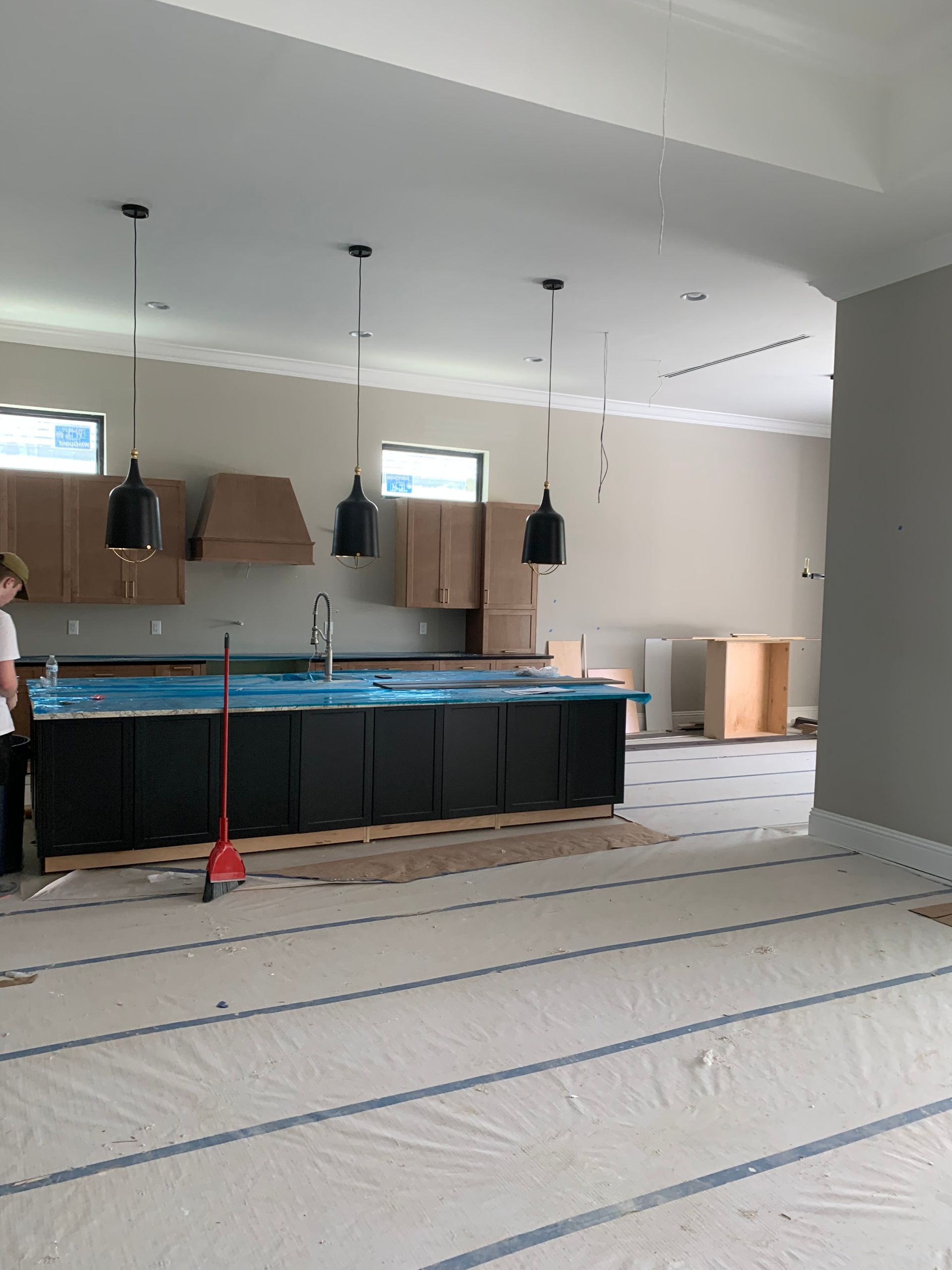 Empty kitchen under renovation with hanging pendant lights, blue-covered counters, and floor protection.