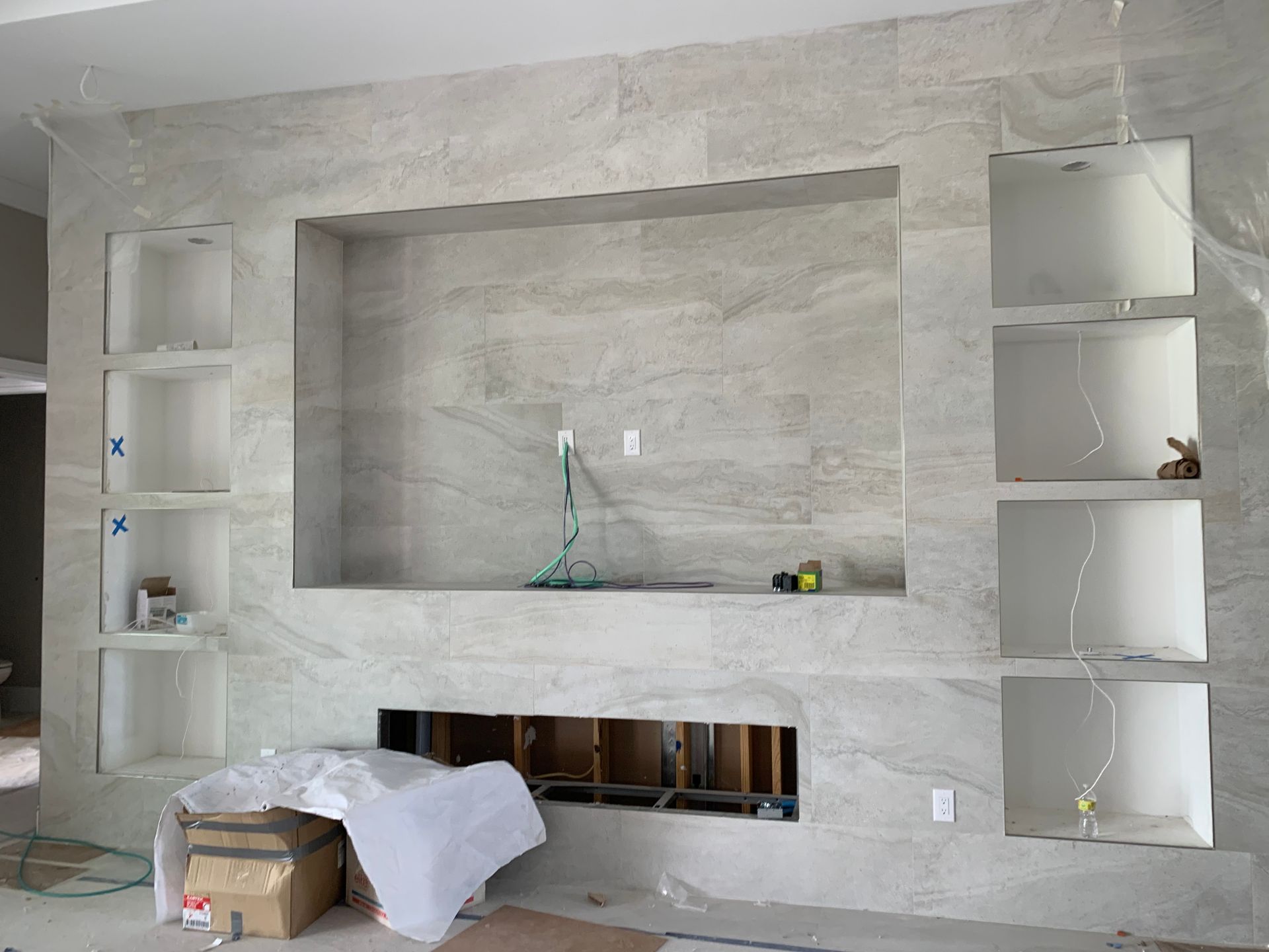 Built-in wall niches with shelves around a large gray stone fireplace in a modern room under renovation