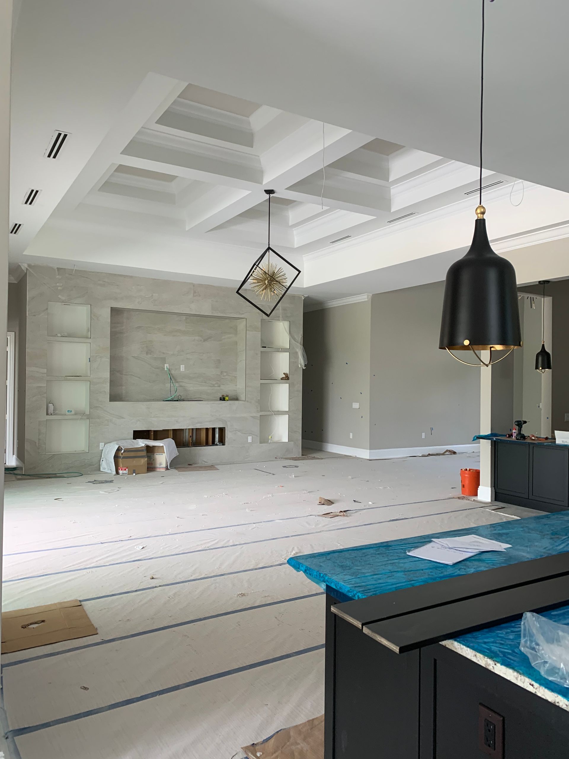 Modern unfinished living room with white walls, skylights, and pendant lights, viewed from a kitchen island