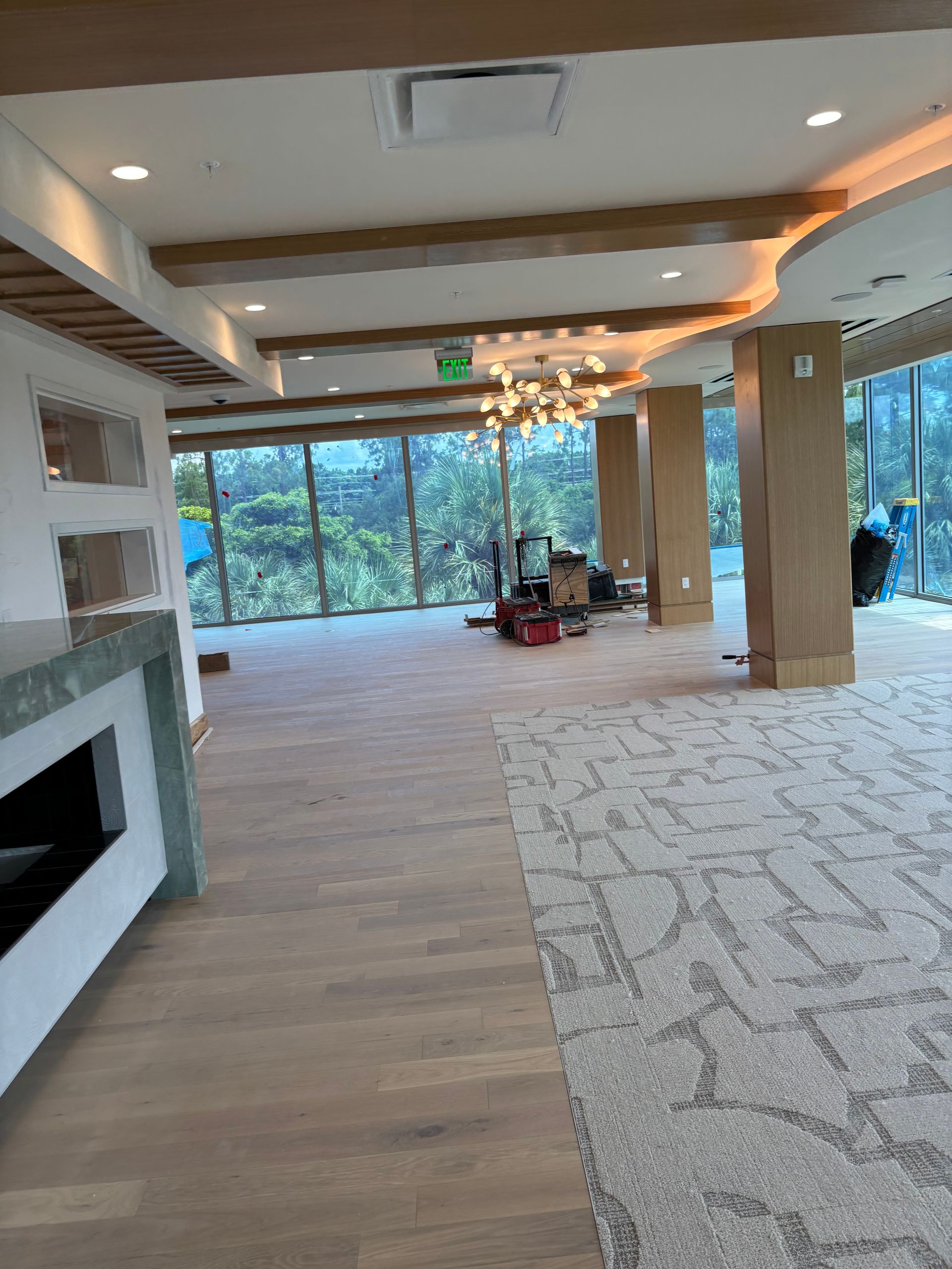 Modern open living room with large windows, wood floors, fireplace, and furniture being moved in