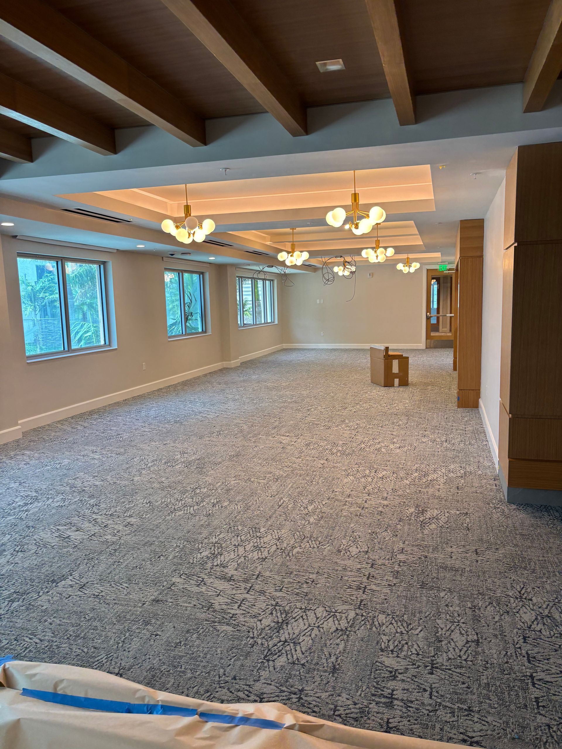 Empty carpeted banquet hall with exposed wood beams, chandeliers, and large windows