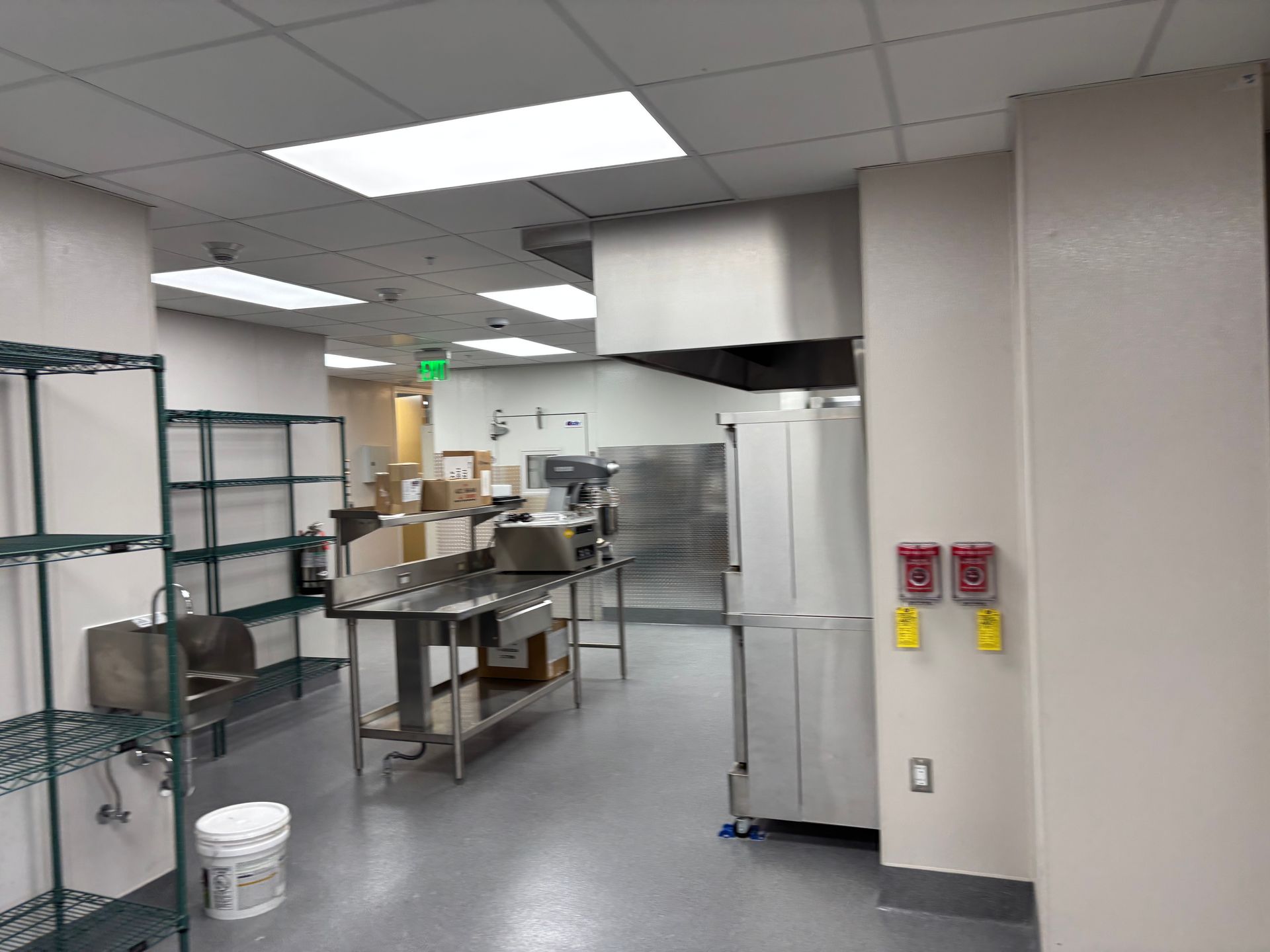 Commercial kitchen with stainless steel counters, shelves, and white walls under bright fluorescent lights