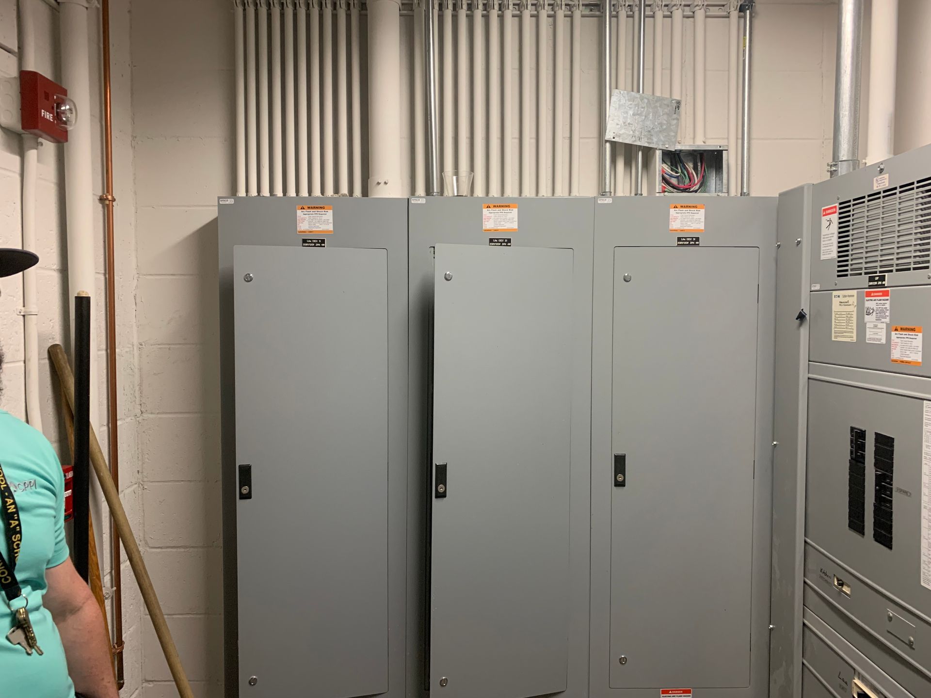 Gray electrical control cabinets in a utility room, with pipes and conduit overhead.