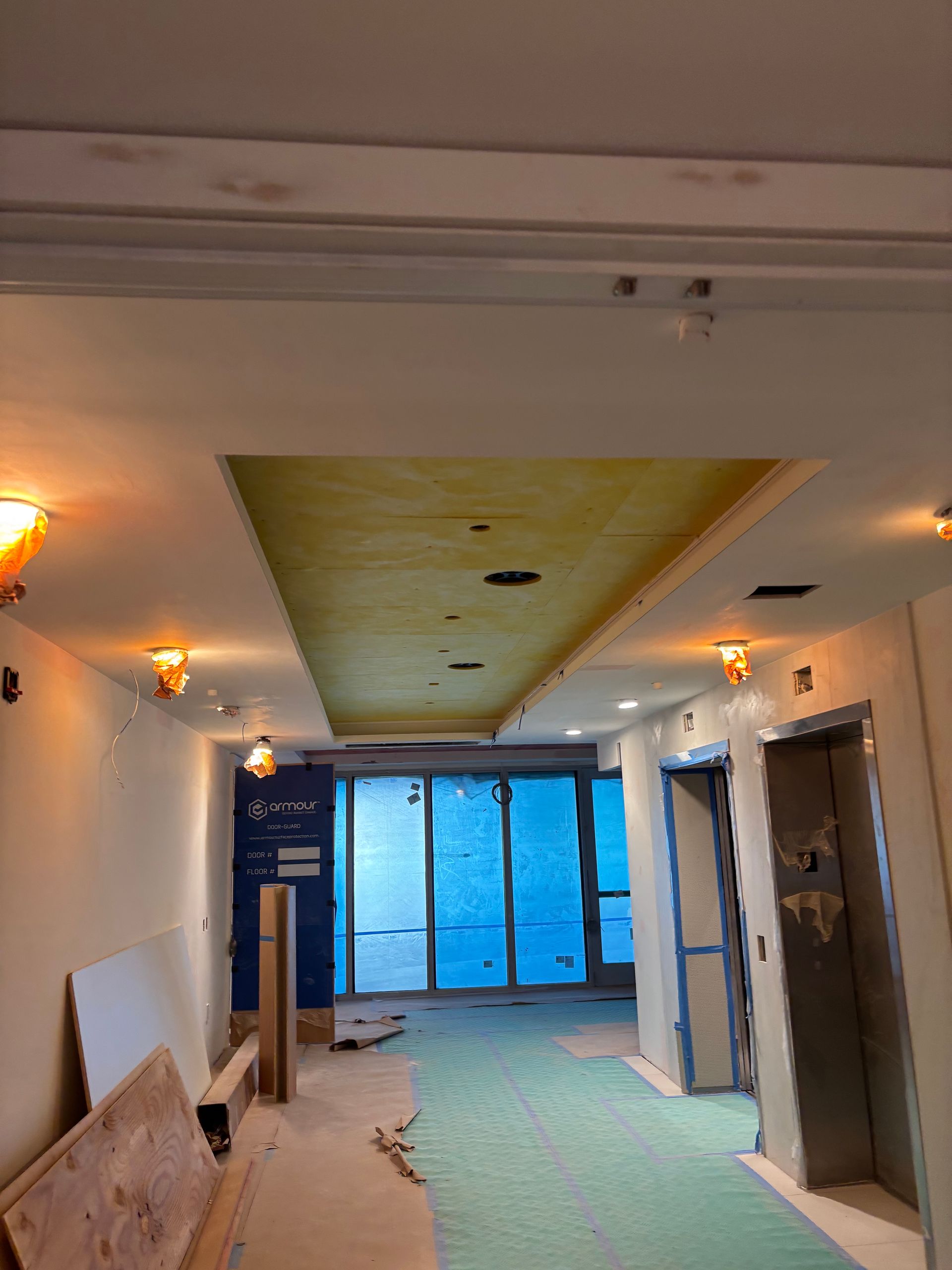 Renovated hallway with blue doors, ceiling cutouts, and construction materials on the floor