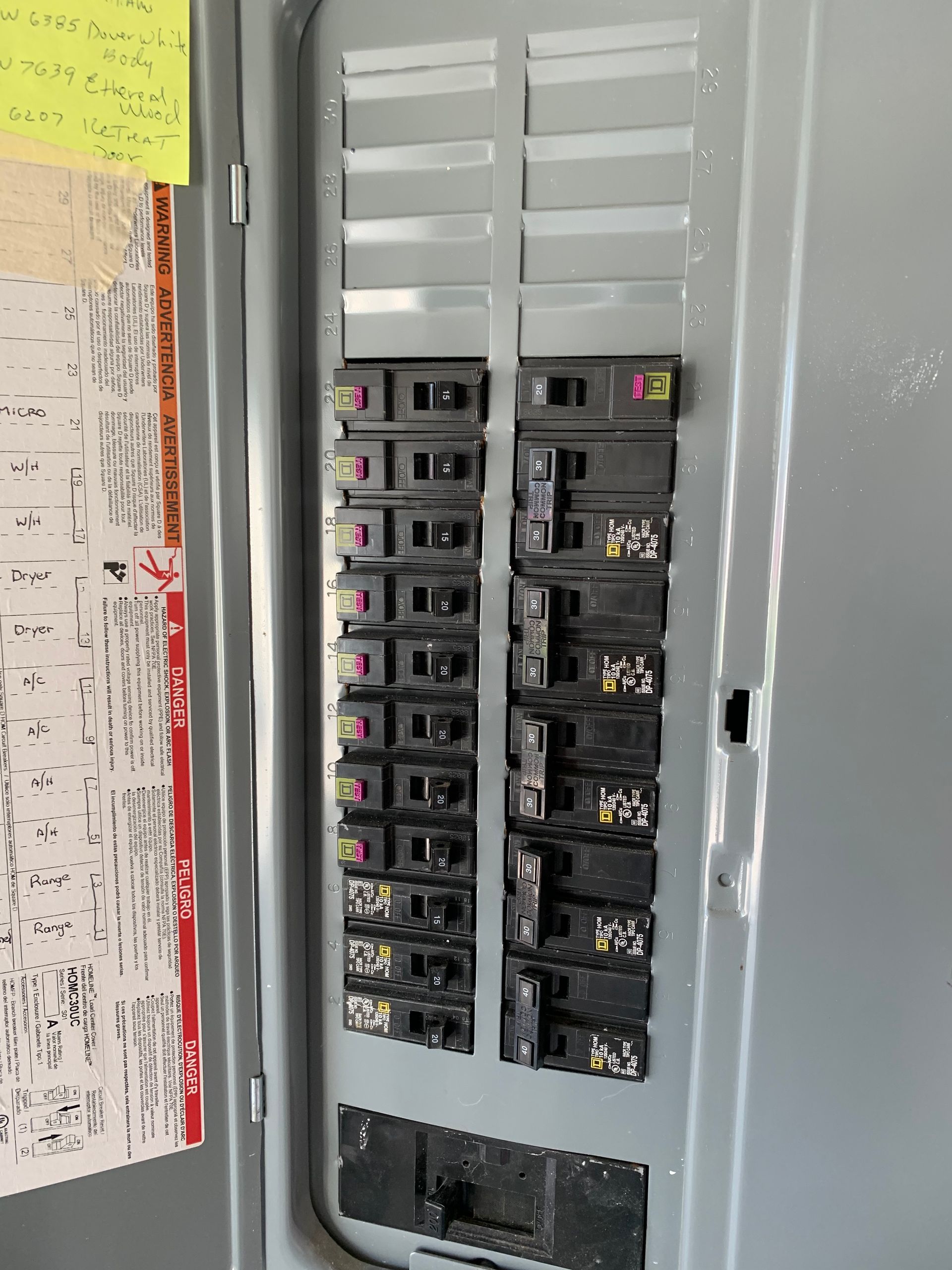 Open electrical breaker panel with rows of black switches and a white door panel nearby