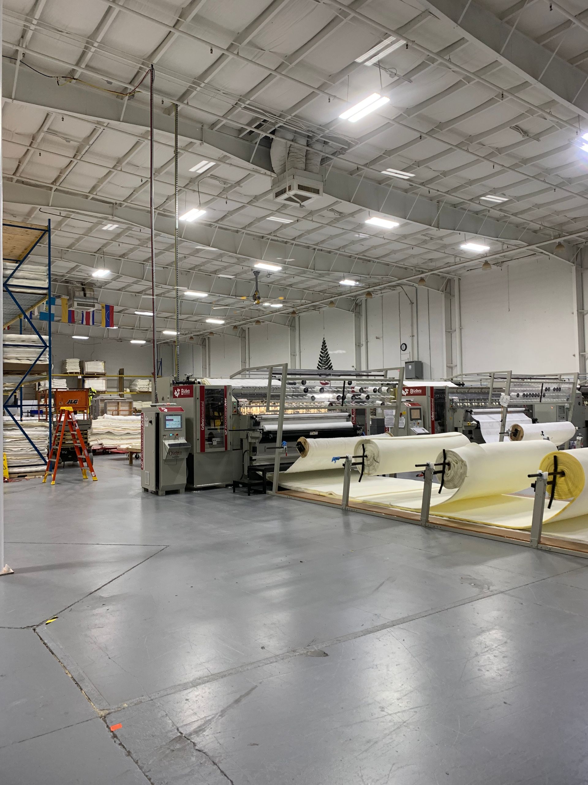 Large industrial warehouse interior with sewing machinery, fabric rolls, and bright overhead lights