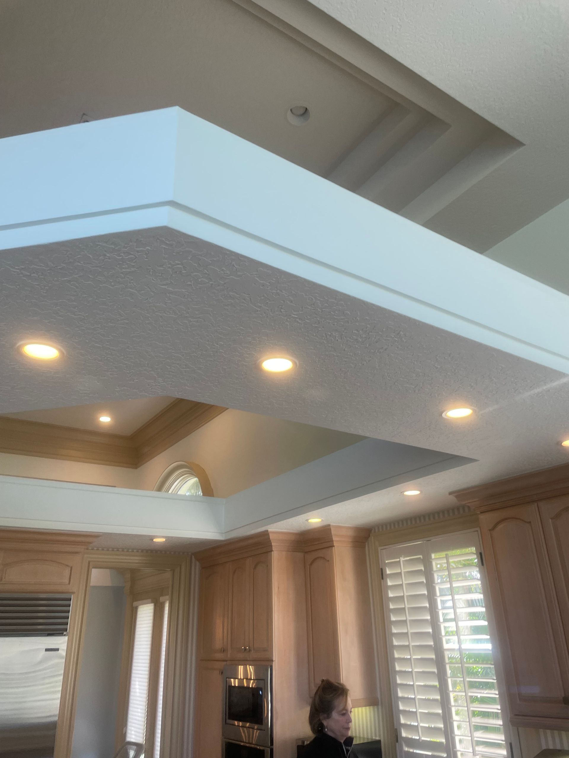 Living room with a tray ceiling, recessed lights, plantation shutters, and wood cabinetry.