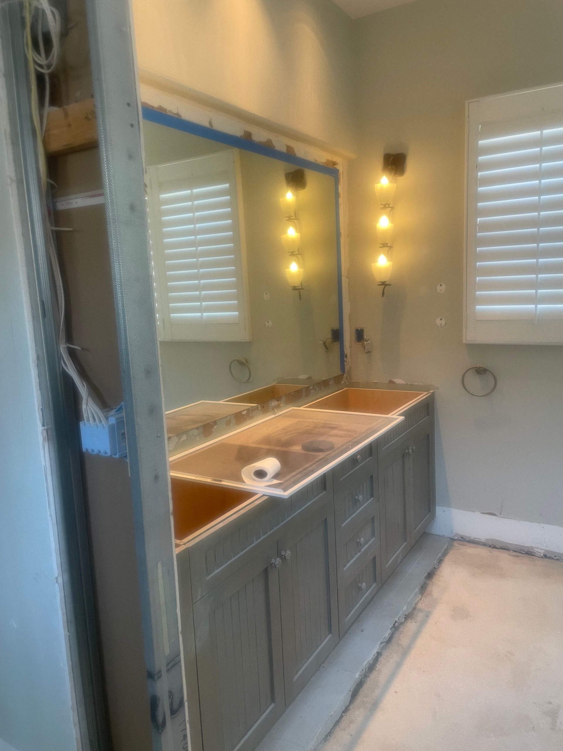 Bathroom vanity with double sinks, large mirror, and wall sconces beside a window with shutters