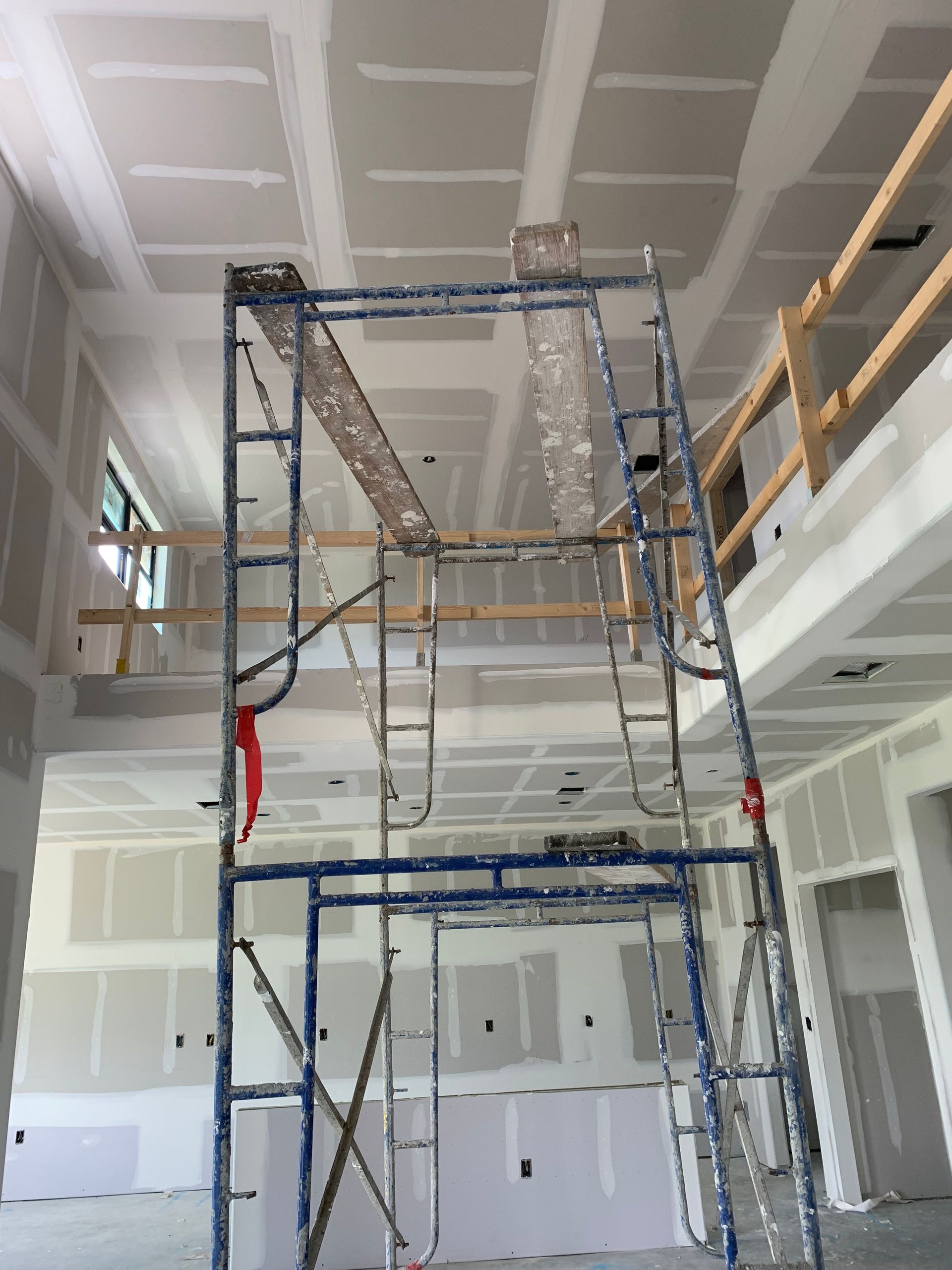 Scaffold in unfinished interior with drywall, ceiling work, and exposed construction materials