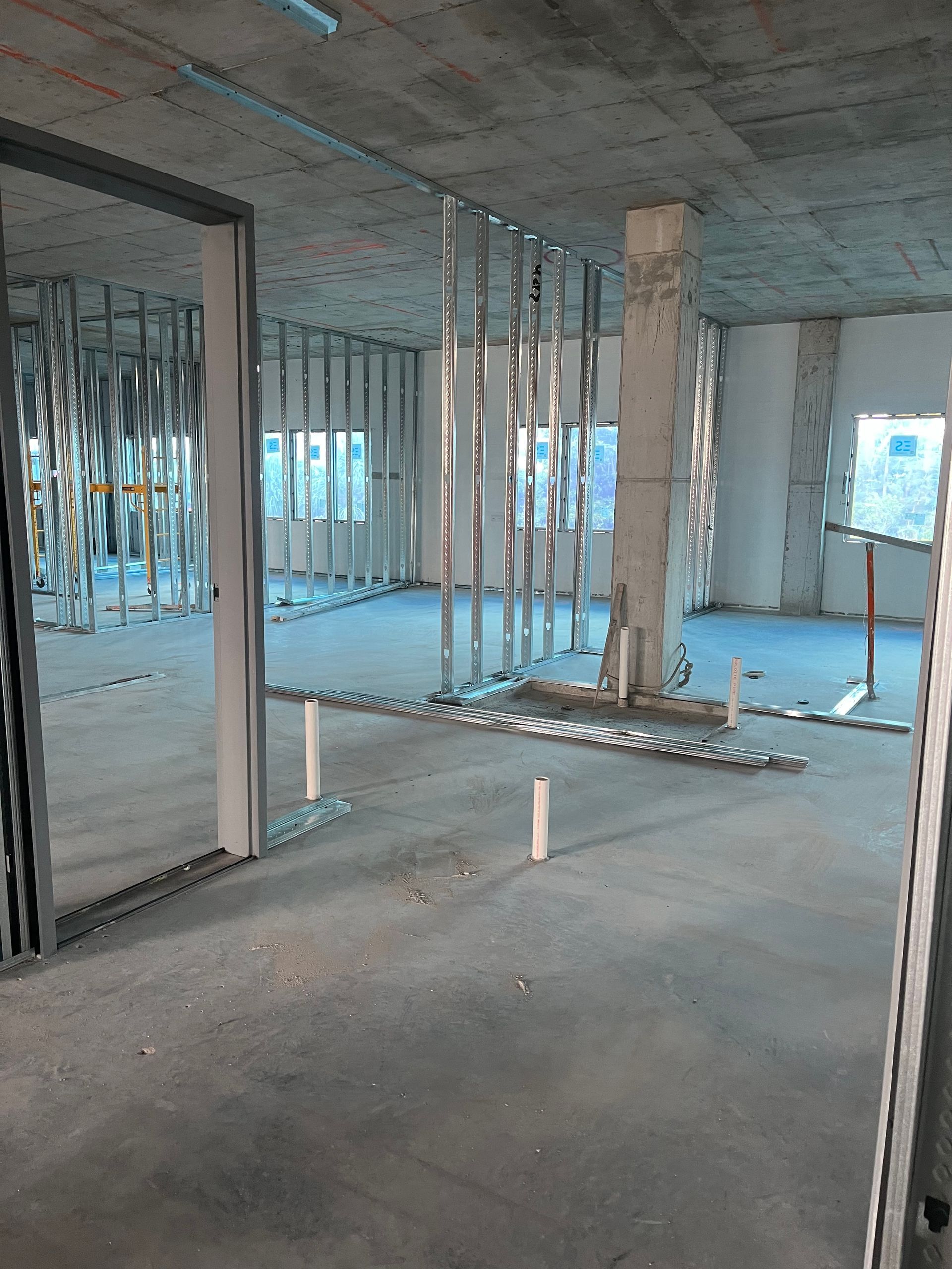 Interior of unfinished building with exposed framing, concrete floors, and hanging electrical wires.