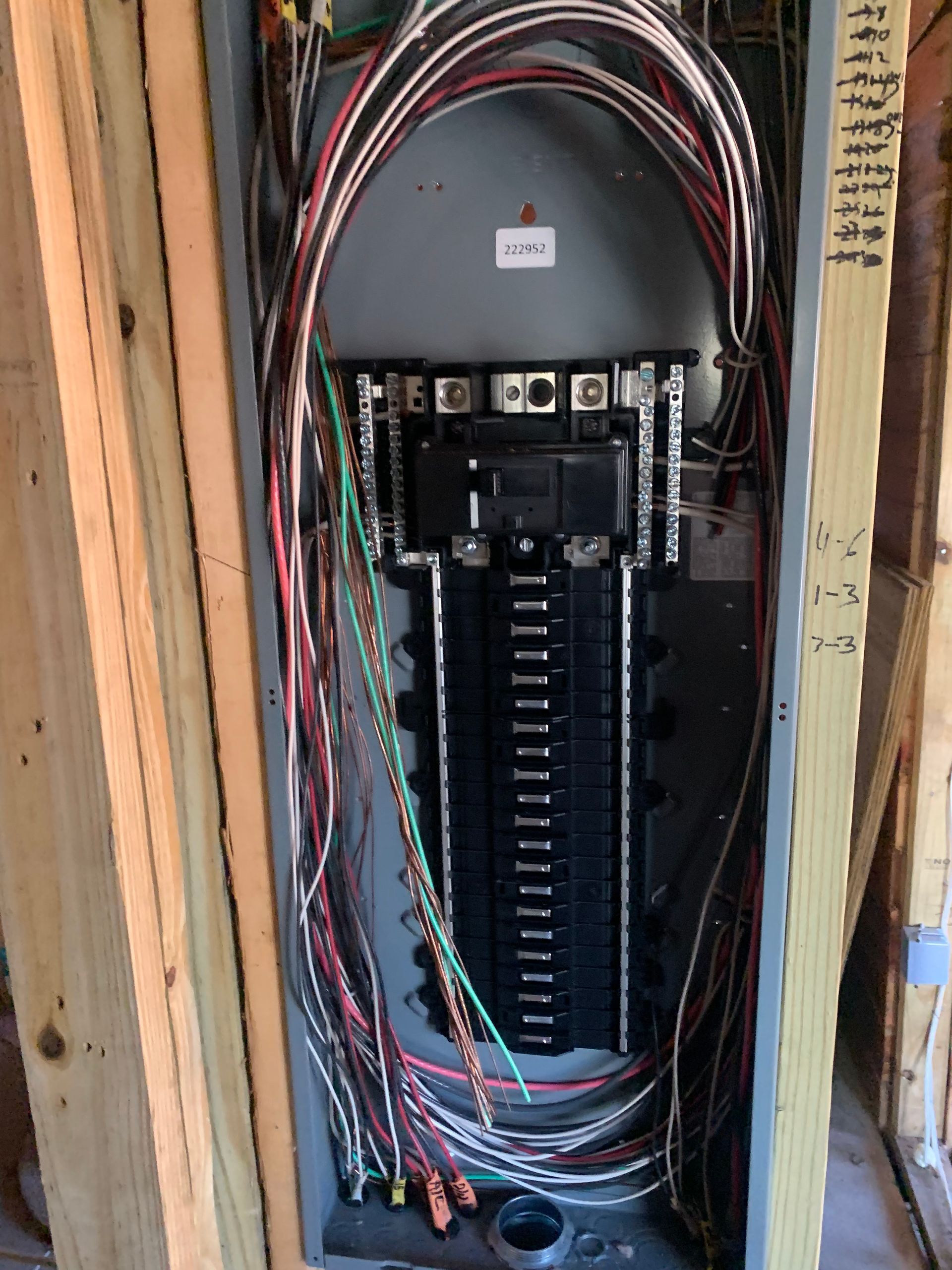 Open electrical panel with bundled colored wires in a wall stud cavity