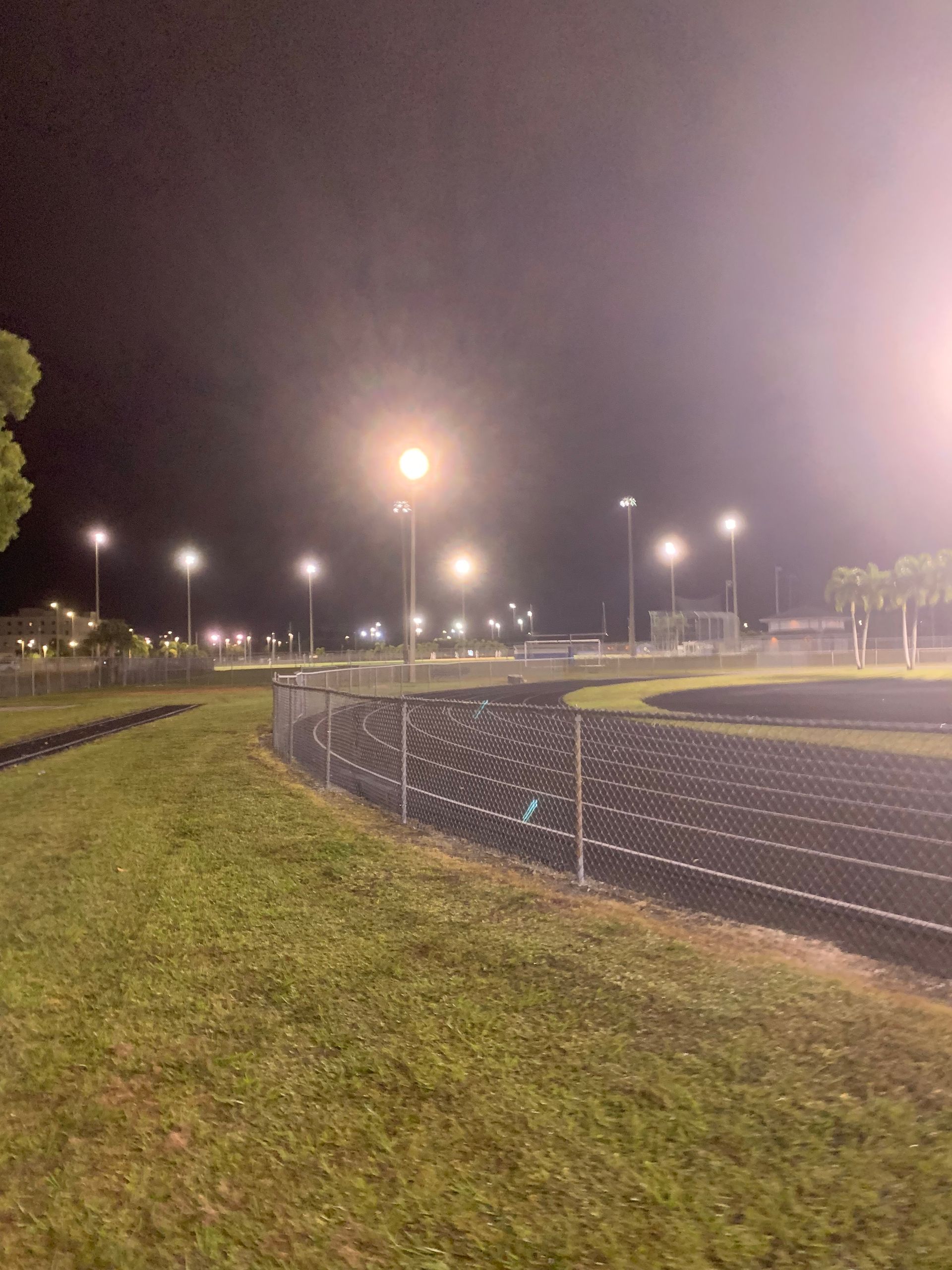 Nighttime stadium track with bright floodlights and a grassy field beside a curved running lane.