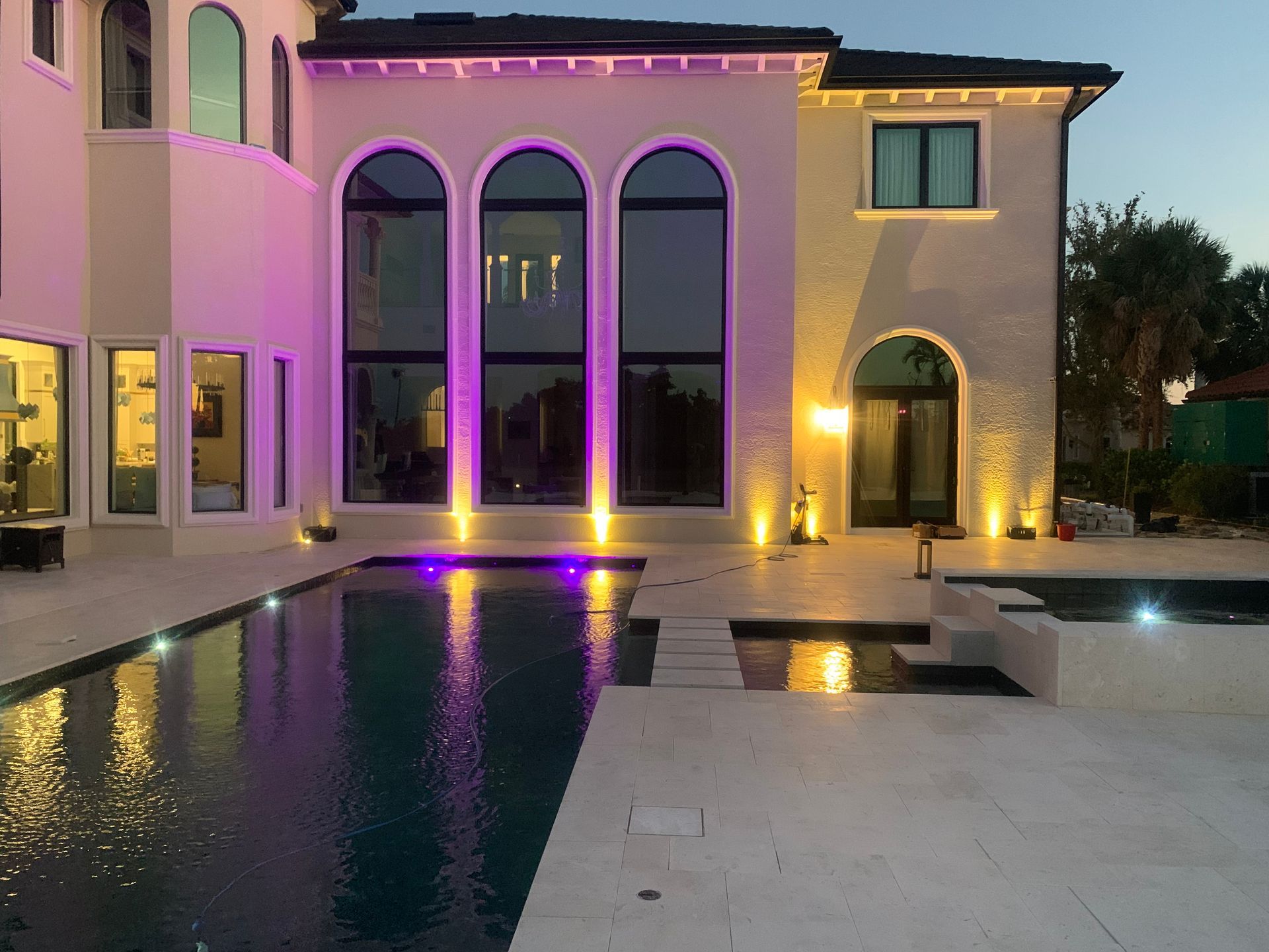 Modern villa with arched windows, lit pool, and purple accent lighting at dusk