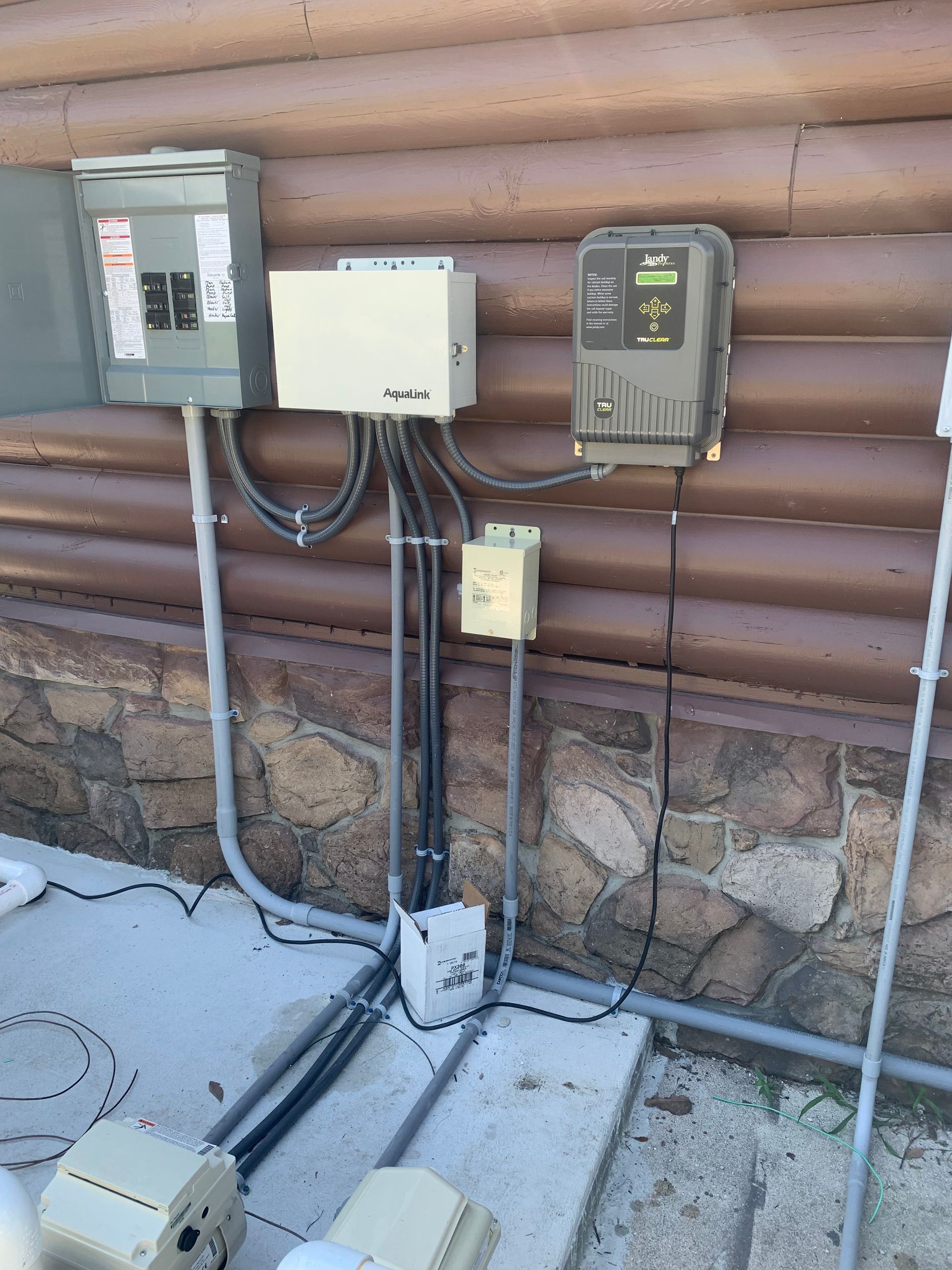 Outdoor electrical meter and utility boxes mounted on a log wall above a stone foundation.
