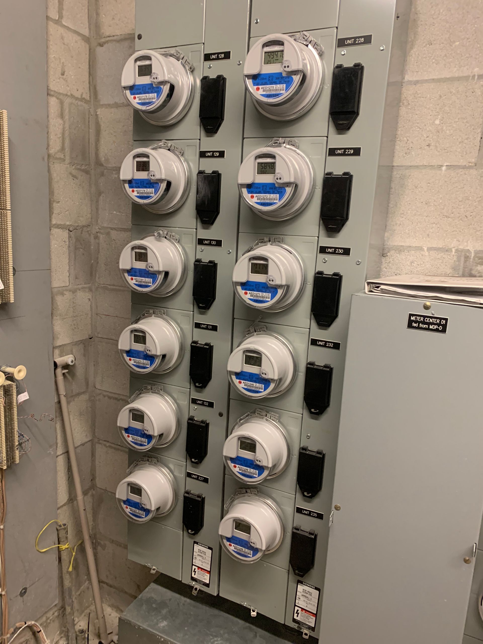 Two rows of electric meters mounted on a wall in a utility room
