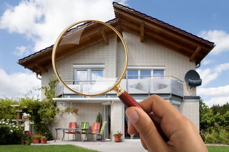 House exterior viewed through a magnifying glass, suggesting home inspection or repair.