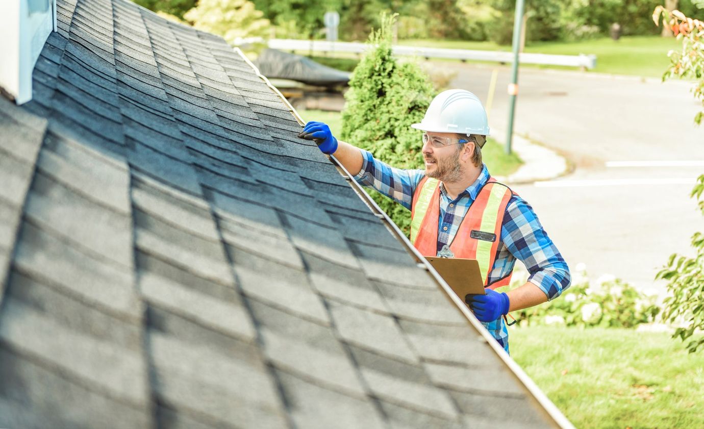 Worker in hard hat and safety vest repairing a shingled roof with a brush tool