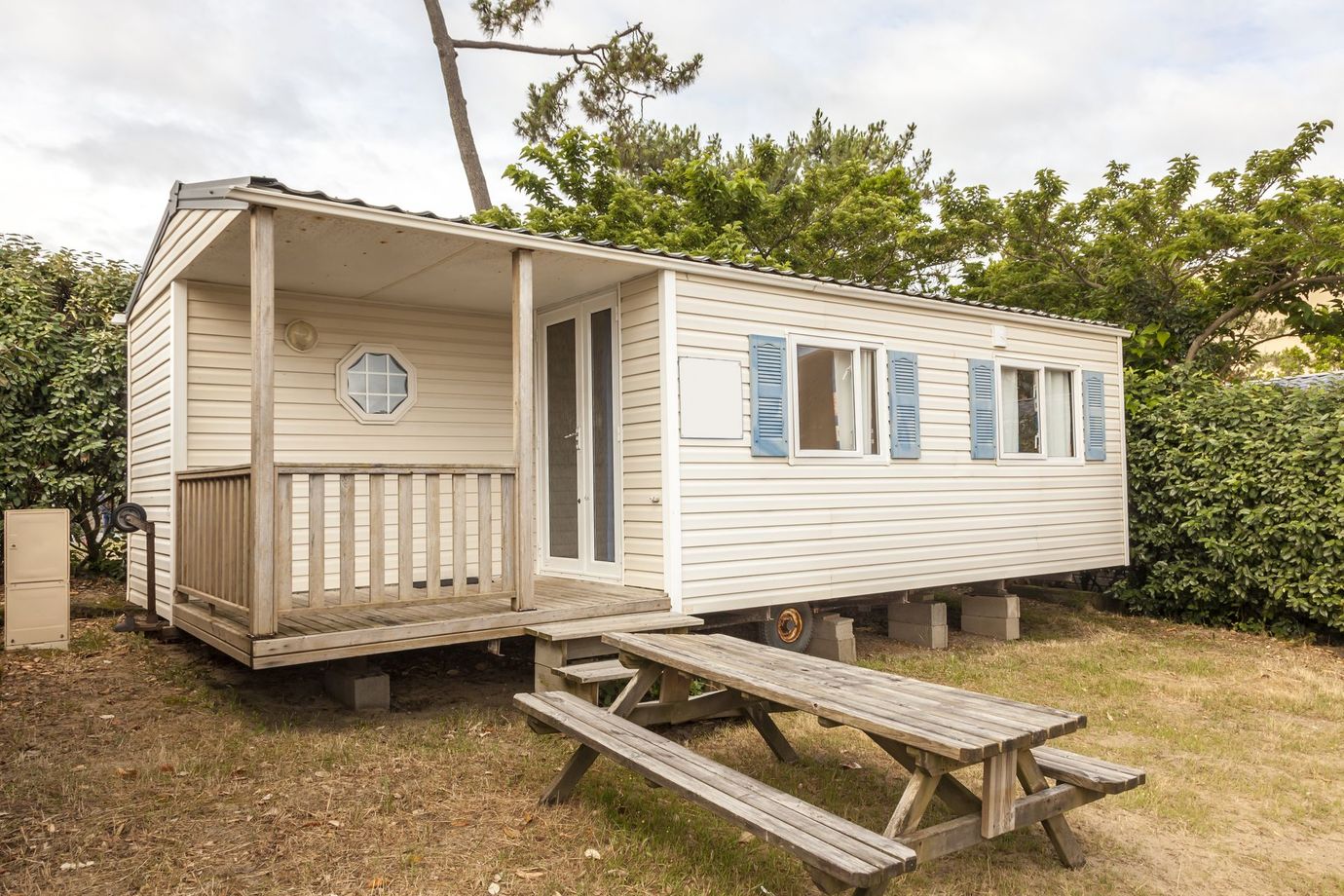 Small white mobile home with blue shutters and a picnic table outside on a grassy lot.