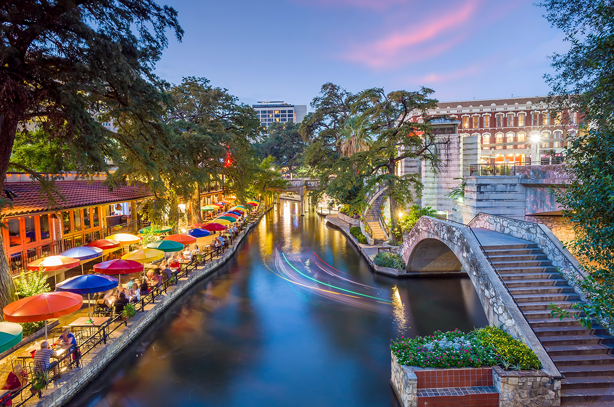 Colorful riverside dining along a canal at dusk, with lit buildings and stone steps beside the water.