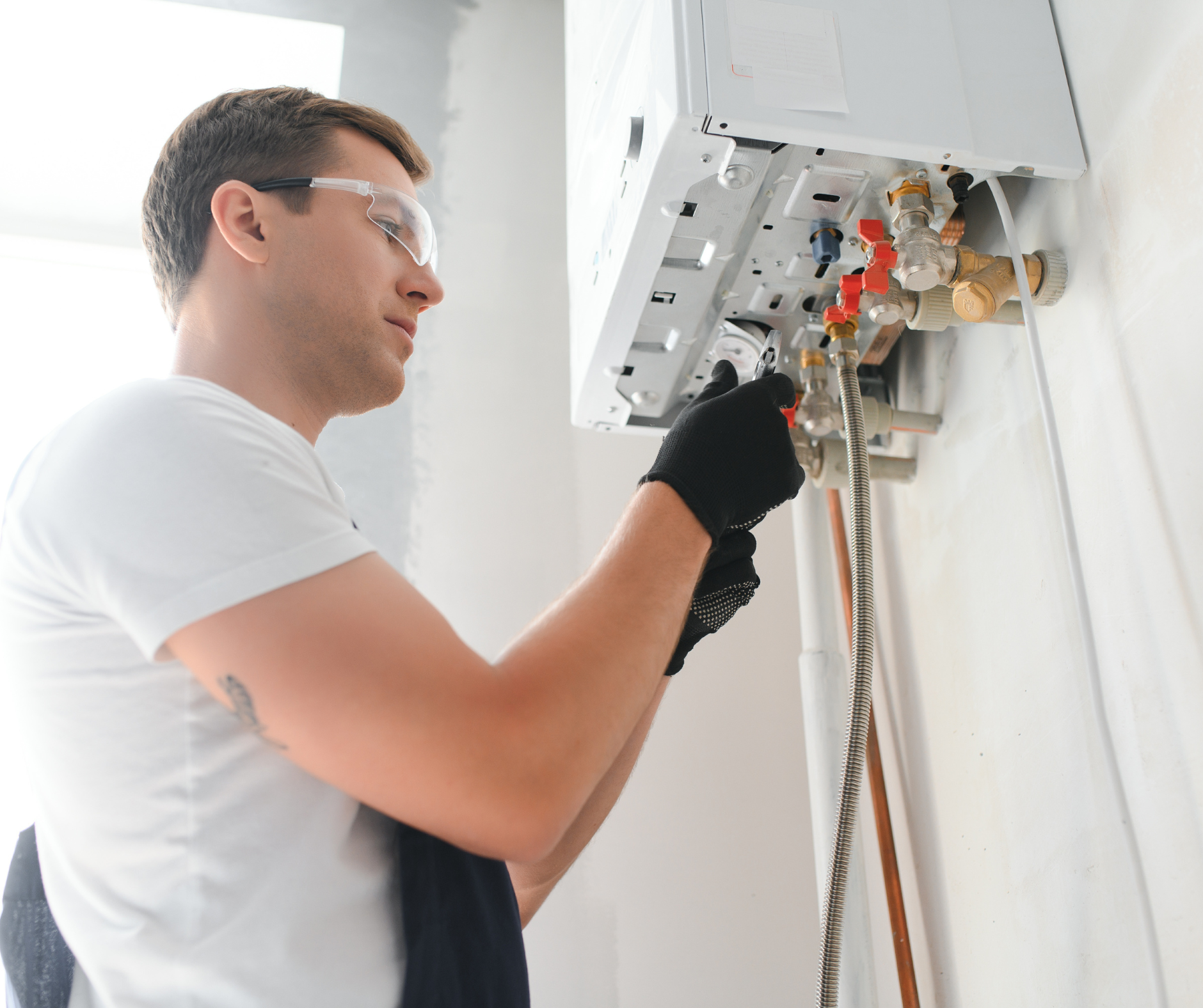 Man in safety glasses and gloves works on a white wall-mounted heating system.