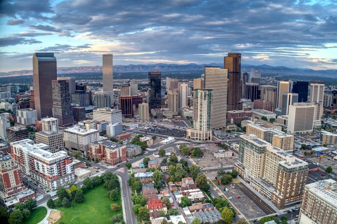 Aerial view of the Denver city skyline at sunset with the Rocky Mountains visible in the distant background.