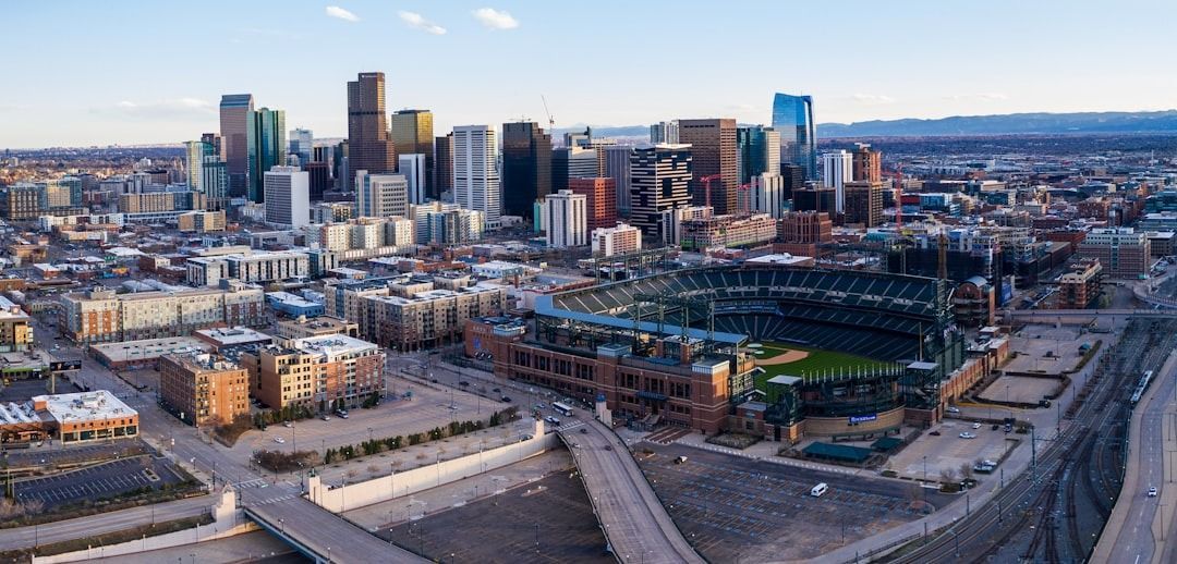 An aerial view of the Denver skyline and Coors Field baseball stadium under a clear blue sky.