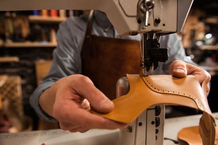 Manos moldeando cuero color tostado bajo una máquina de coser en un taller