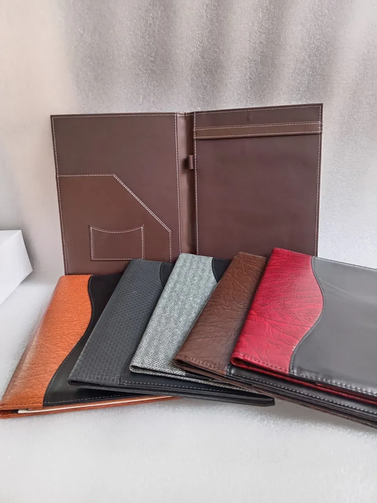 Varias carteras de cuero marrones, negras, grises, rojas y naranjas colocadas delante de una carpeta marrón