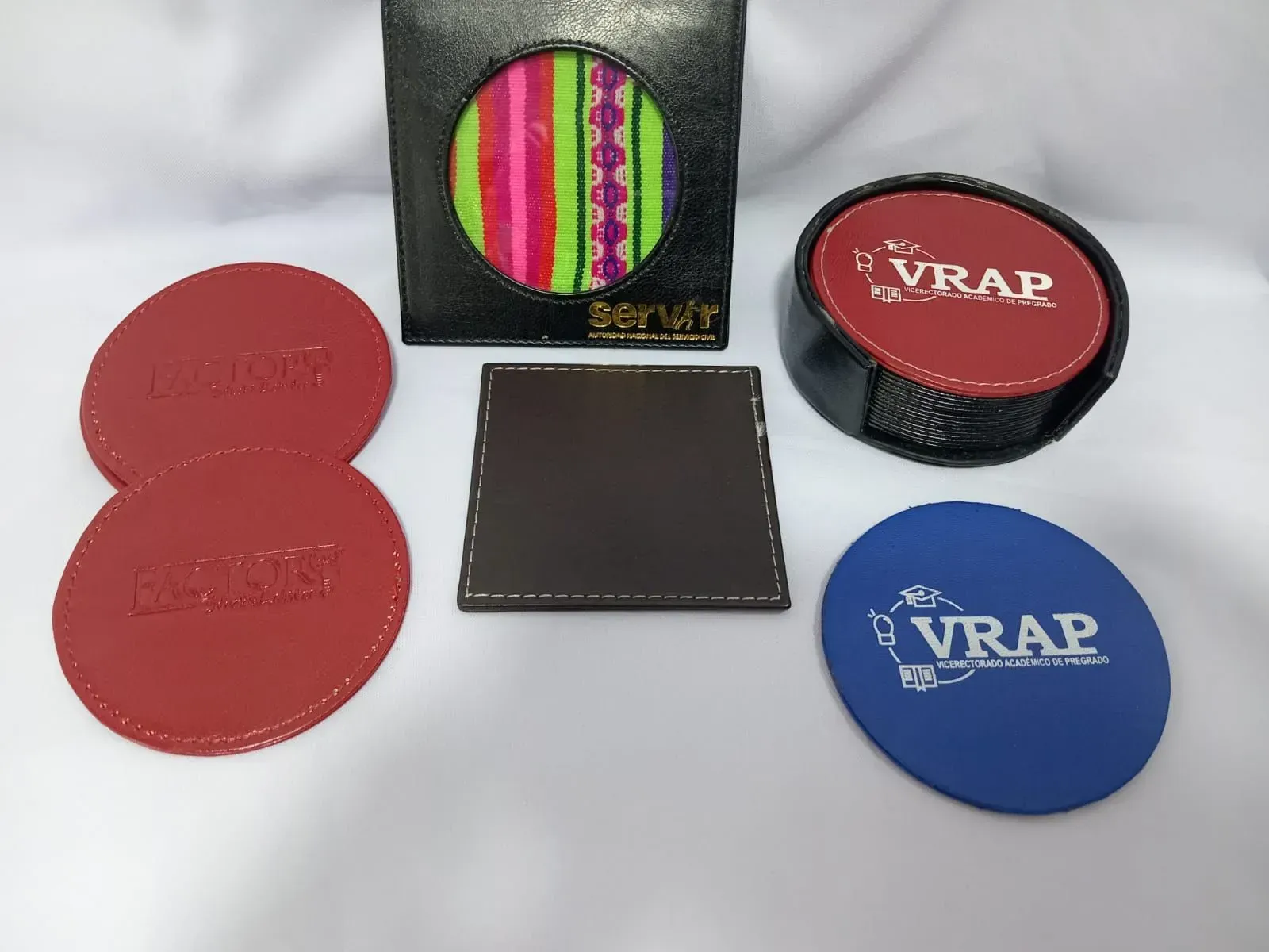 Posavasos redondos variados con marca y un posavasos cuadrado, en rojo, azul y negro, sobre un fondo claro