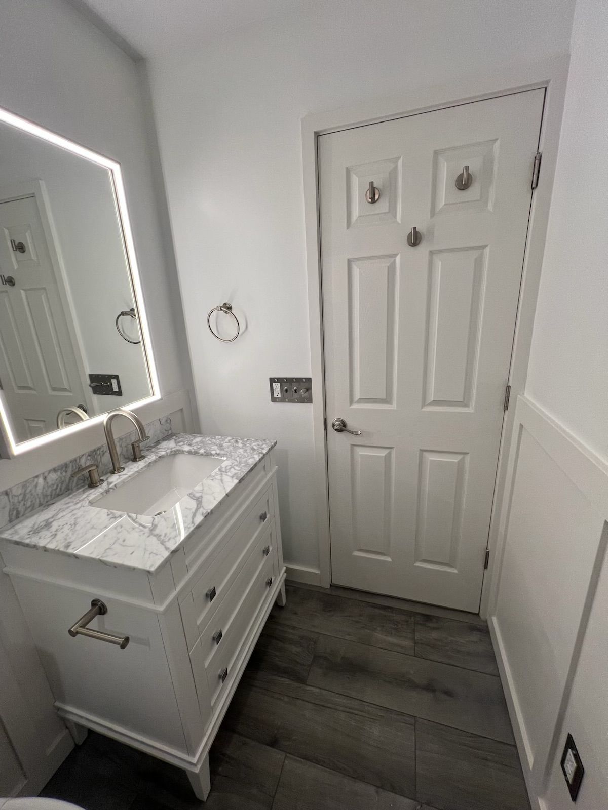 A bathroom with a sink , mirror and door.
