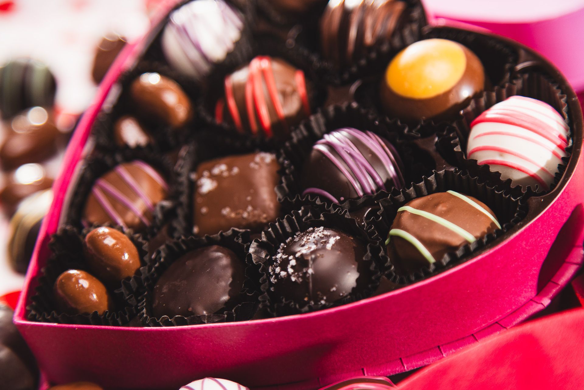 A heart-shaped box filled with an assortment of dark, milk, and white chocolate truffles with decorative drizzles.