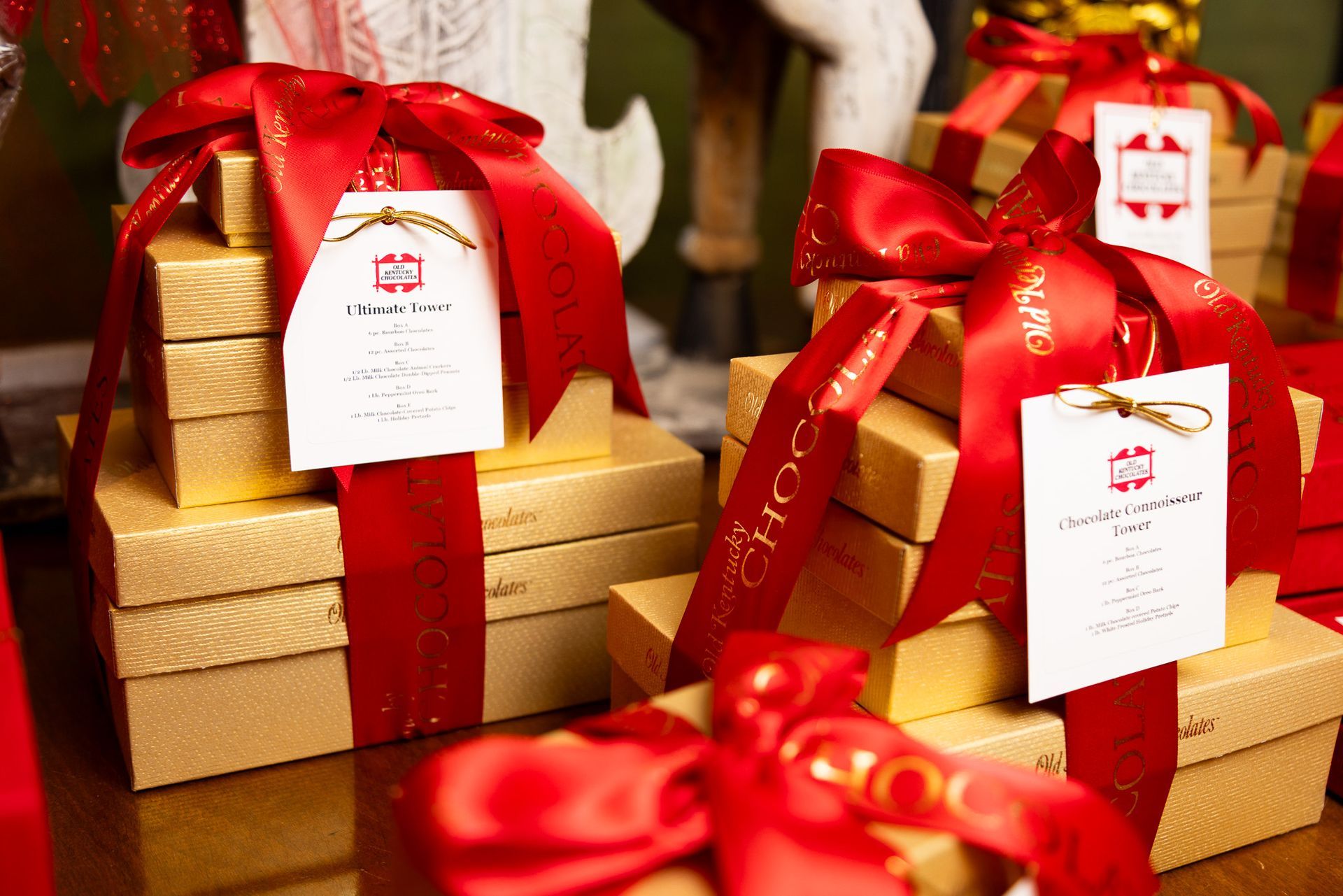 Stacks of gold gift boxes tied with red ribbons and branded white tags on a surface.