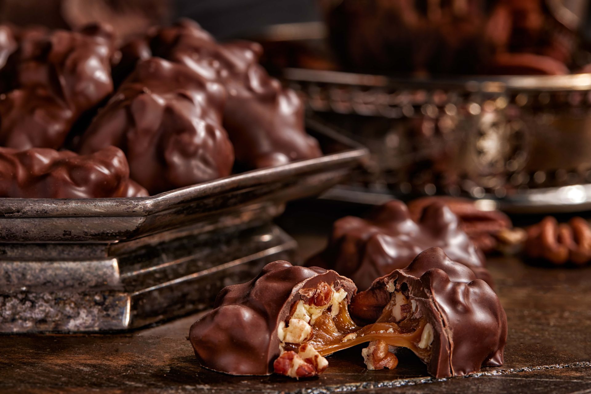 Chocolate pecan clusters with caramel filling on a silver tray and wooden surface.